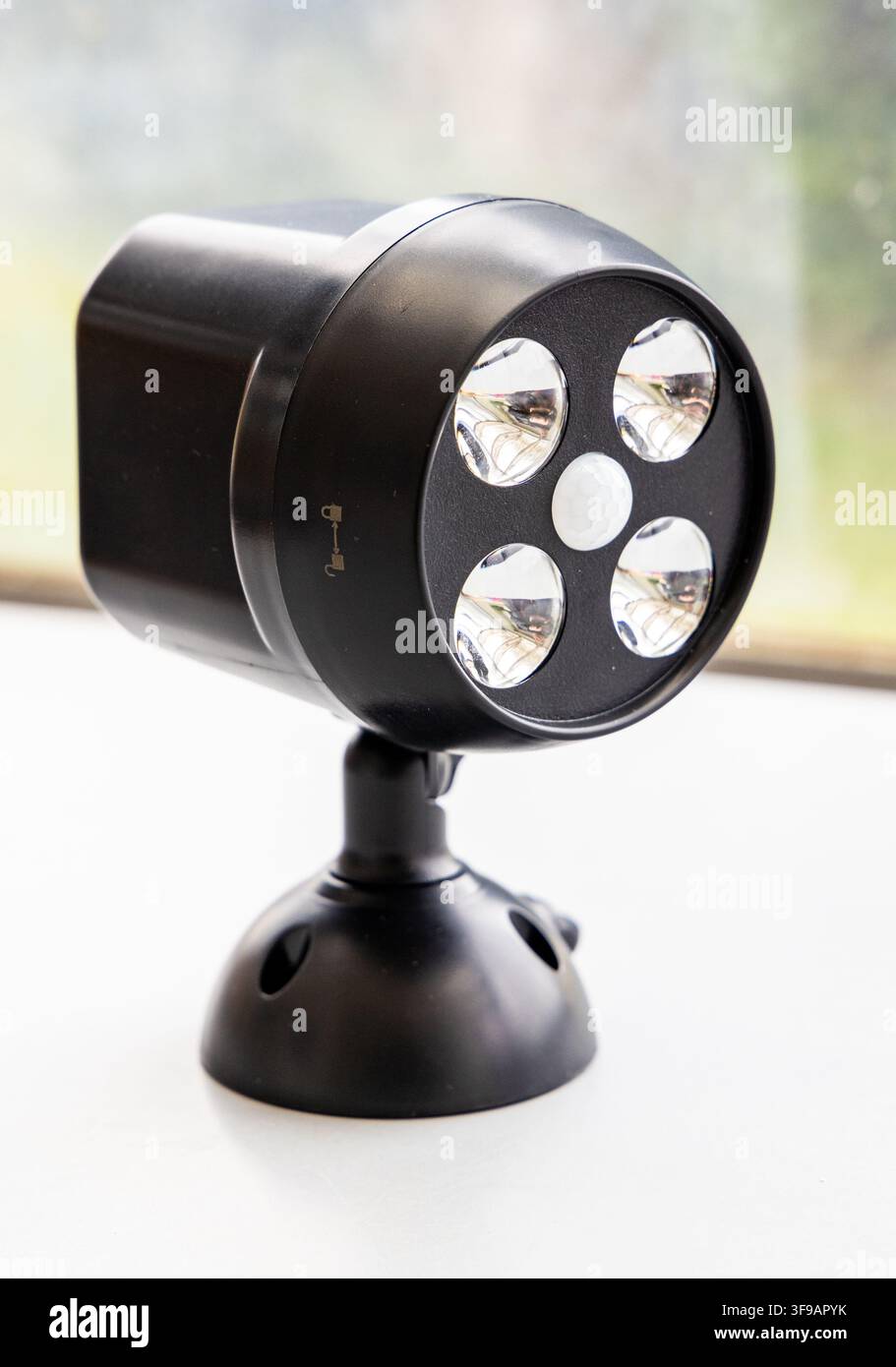 A black LED motion sensor security light sits on a white surface Stock Photo