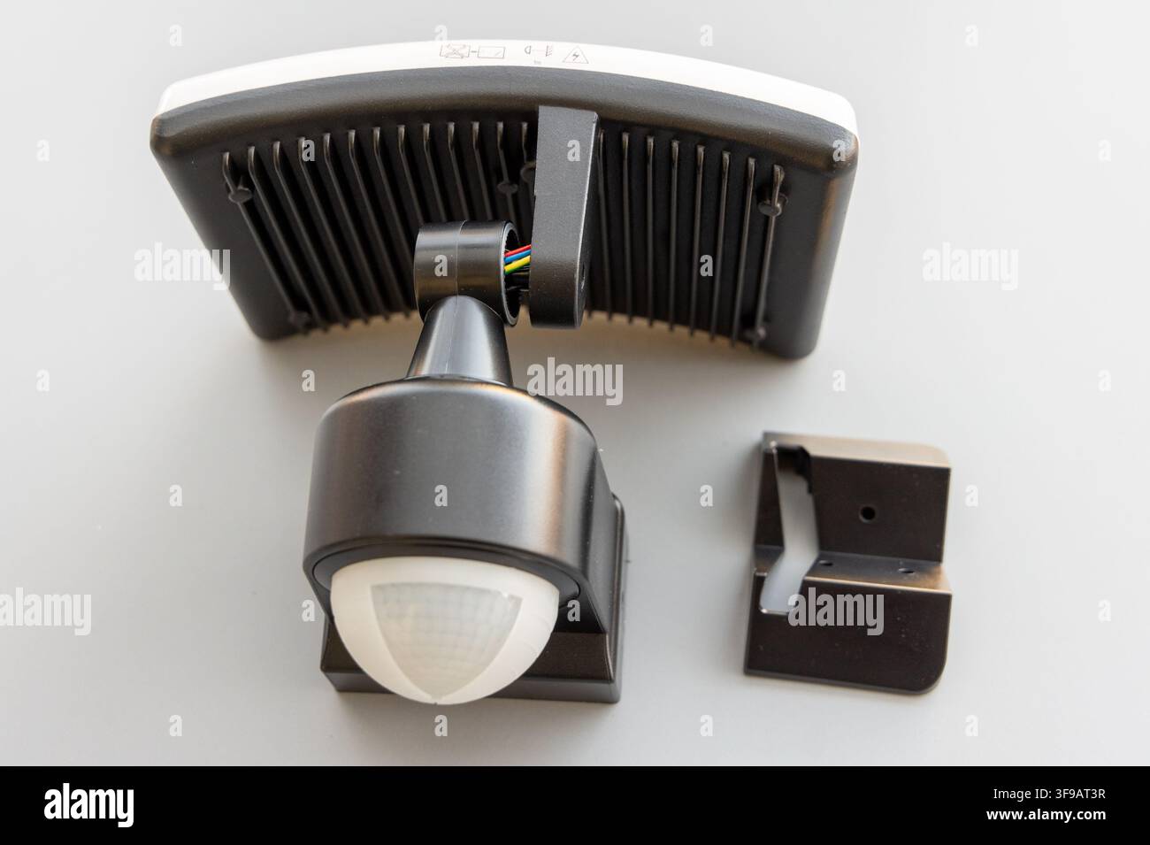A black motion sensor LED floodlight with its bracket on white Stock Photo