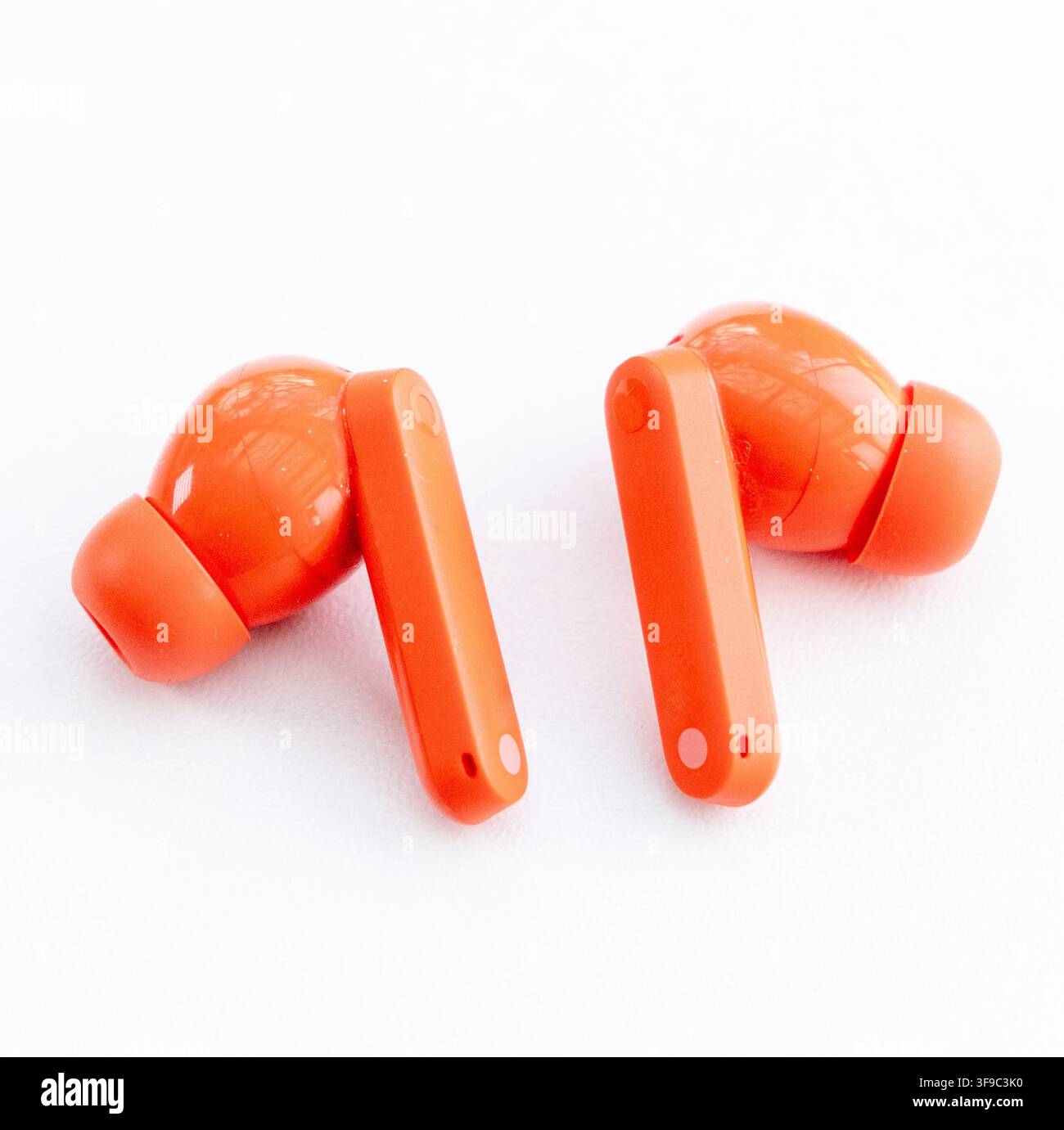 Two vibrant orange wireless earbuds rest on a clean white surface Stock Photo