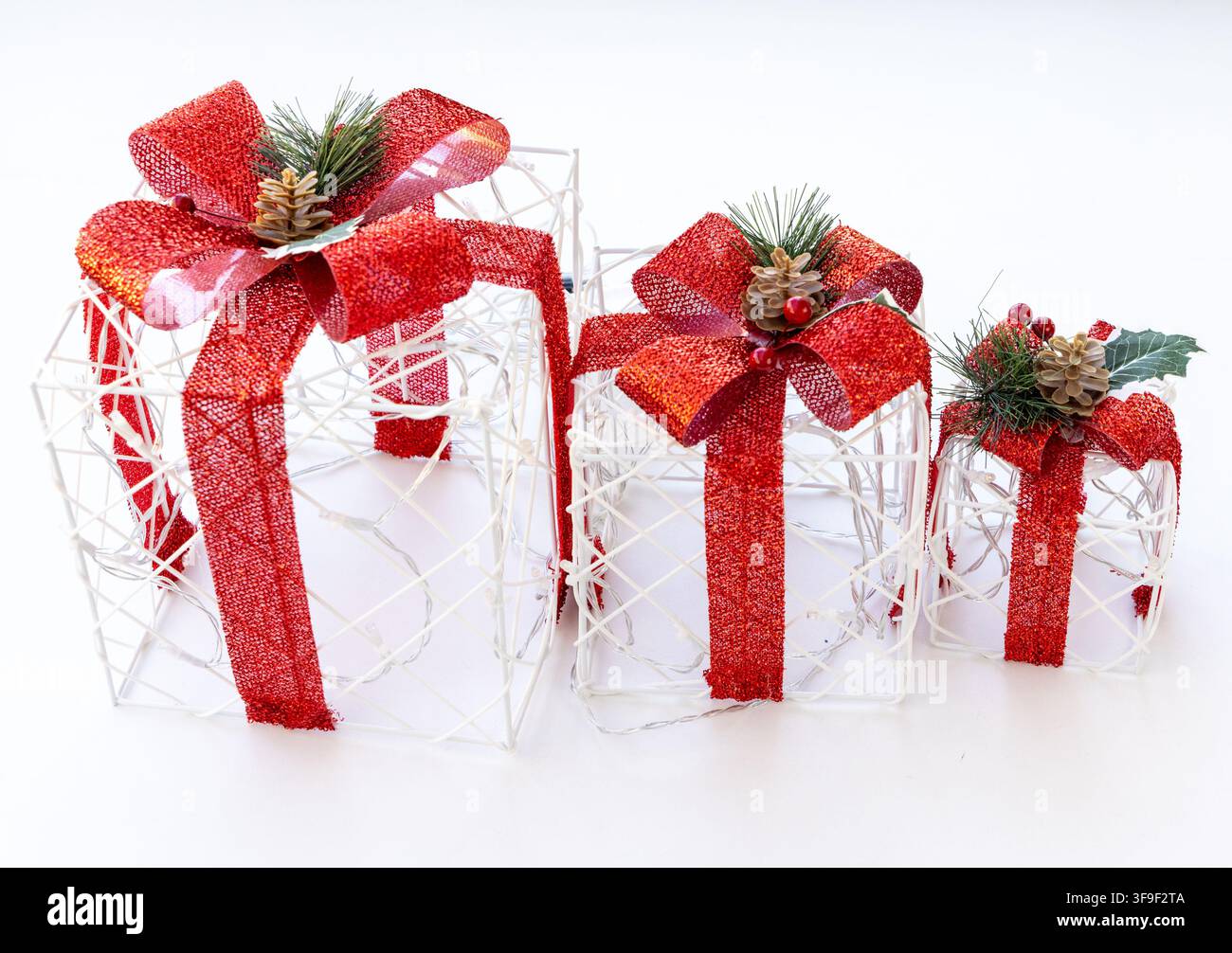 Three glowing white wire gift boxes with red bows sit on white Stock Photo