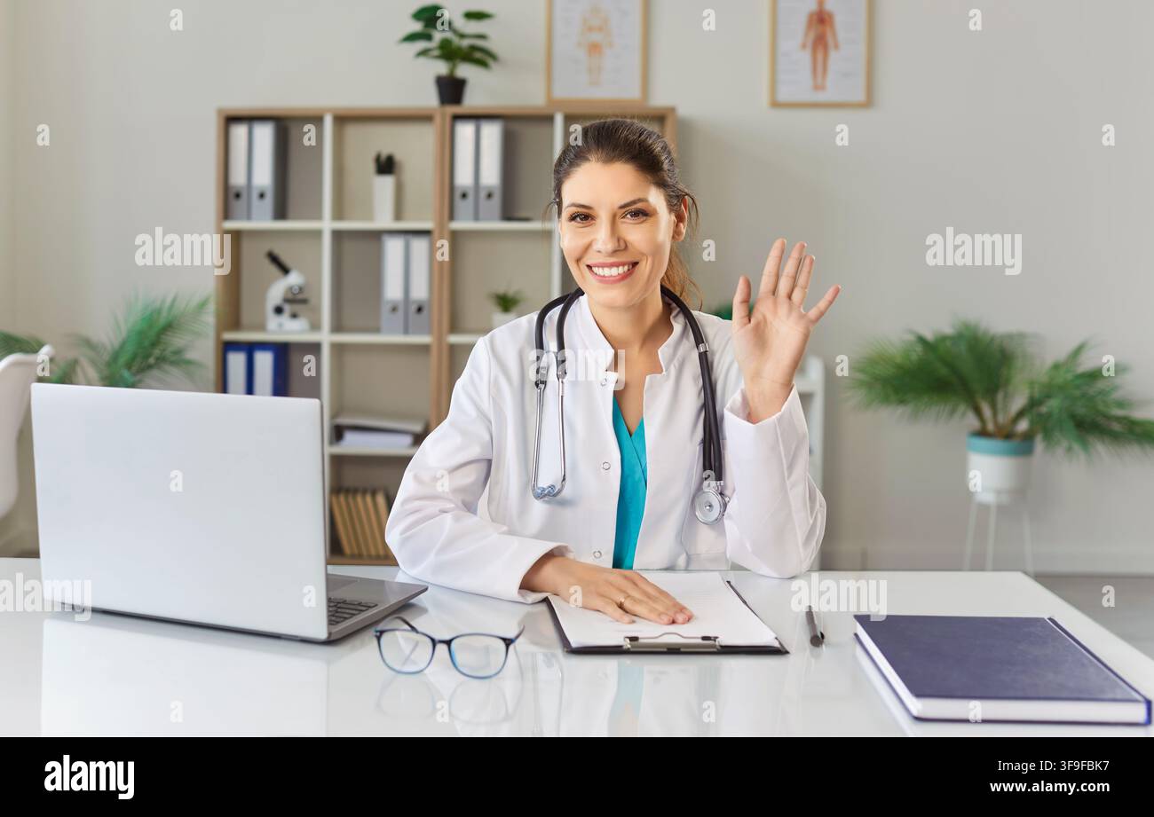 Friendly female doctor looking at camera having online video call or conference in office. Stock Photo