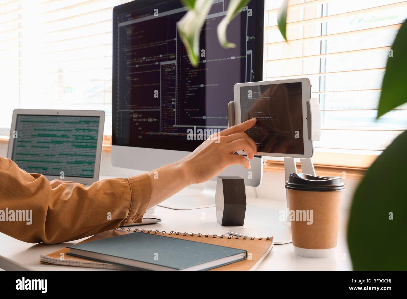 Programmers hand touching a tablet screen with code, multiple monitors displaying software development, modern office workspace Stock Photo