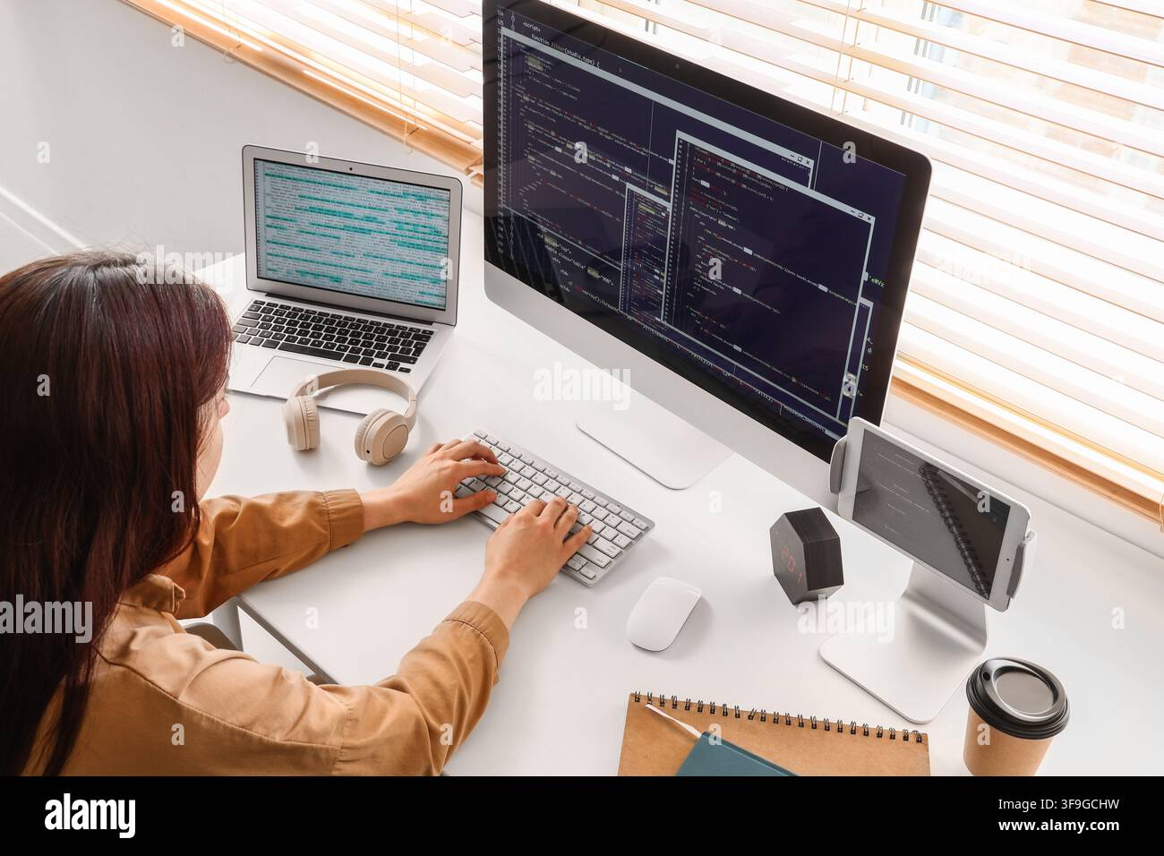 Female programmer coding on multiple screens at a modern home office desk, software development and remote work Stock Photo
