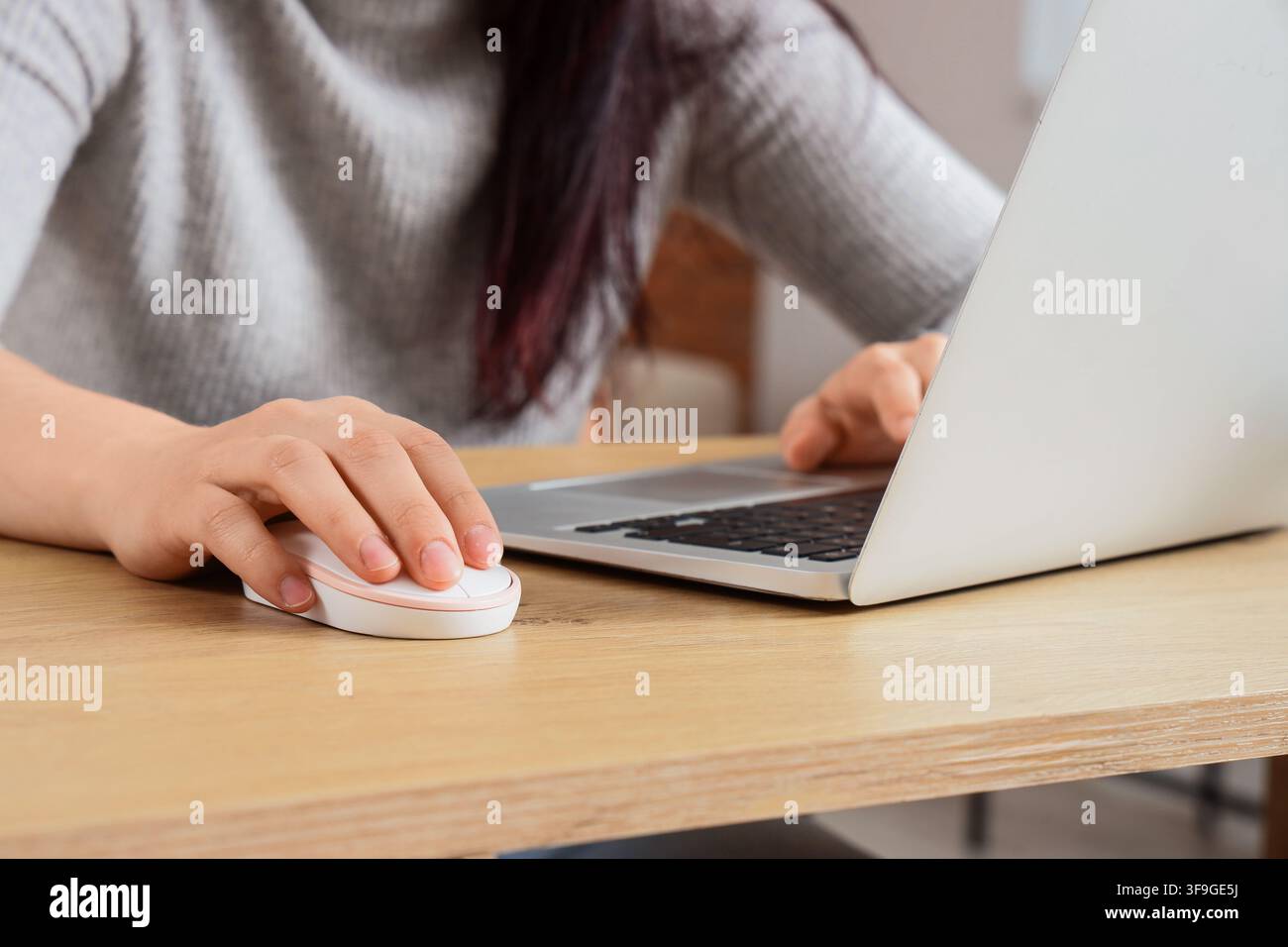 Womans hand using a white computer mouse on a wooden desk with a laptop, remote work and digital communication concept, Modern technology and connecti Stock Photo