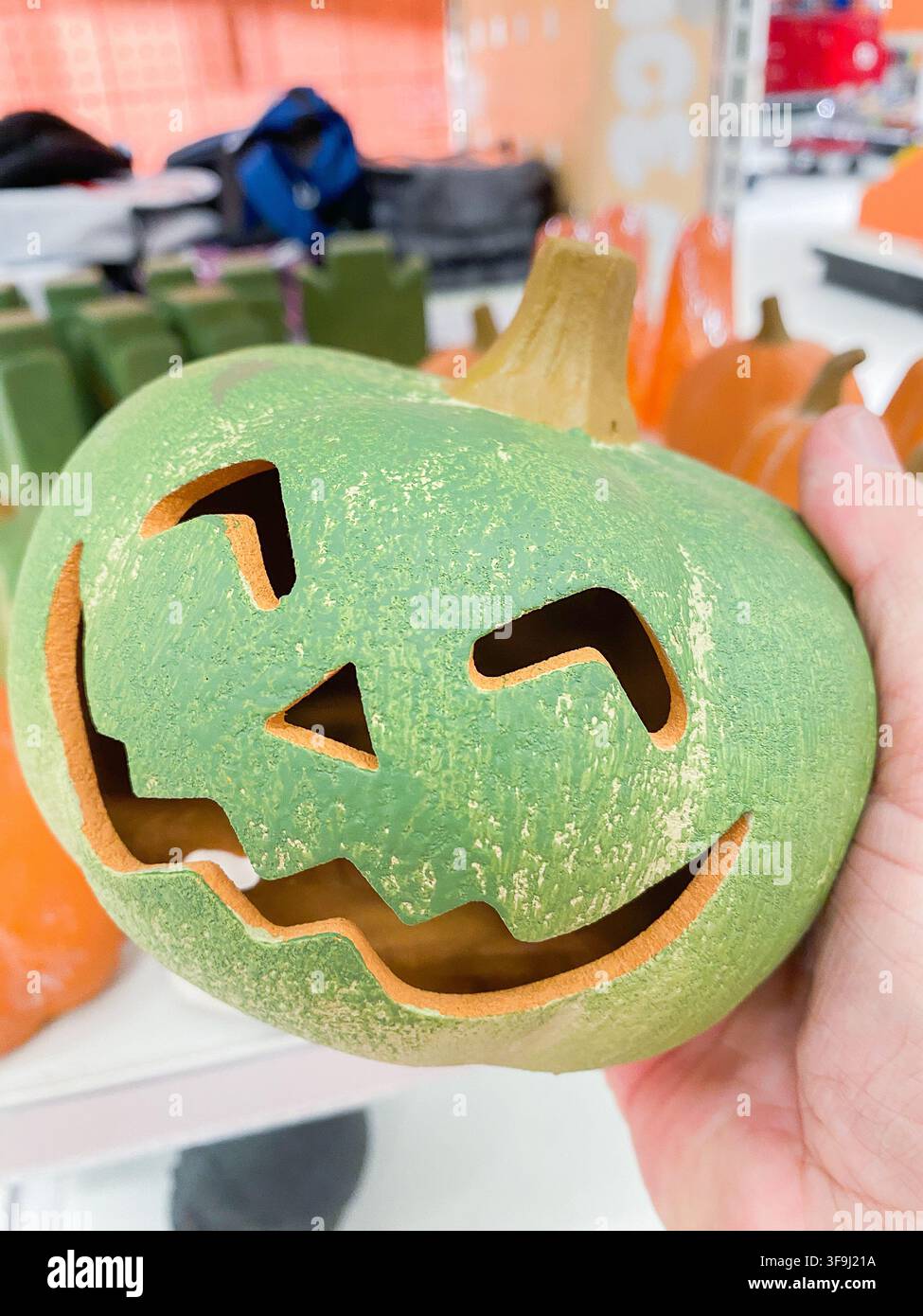 A hand holding a green ceramic jack-o-lantern pumpkin decoration for Halloween - August 8. 2026, Portland Oregon, USA Stock Photo