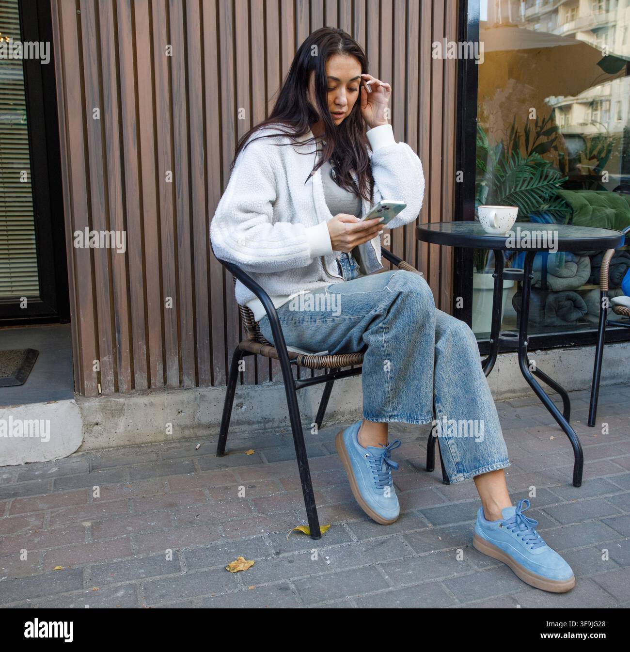 Nice woman sitting in street cafe using smartphone and drinking coffee Stock Photo