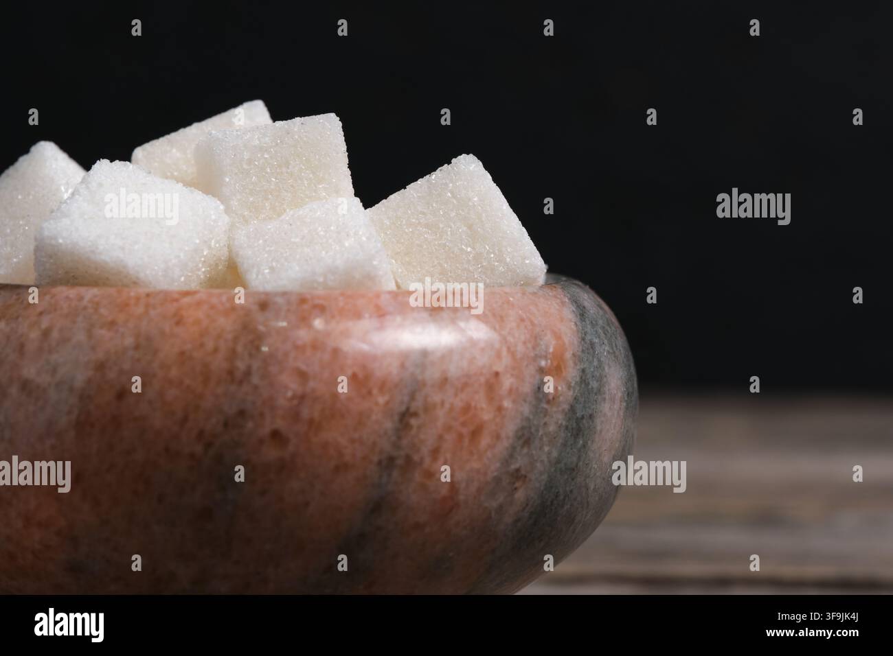Macro close up view white sugar cubes in marble bowl on rustic wooden table surface Stock Photo