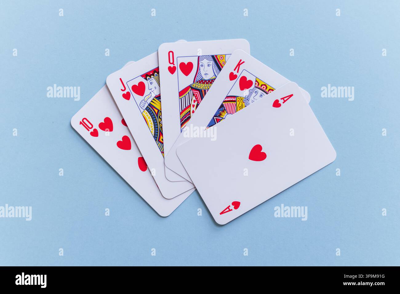 Royal flush hand of heart playing cards fanned out on a pastel light blue background. Minimalist flat lay stock photo representing luck, victory, casi Stock Photo