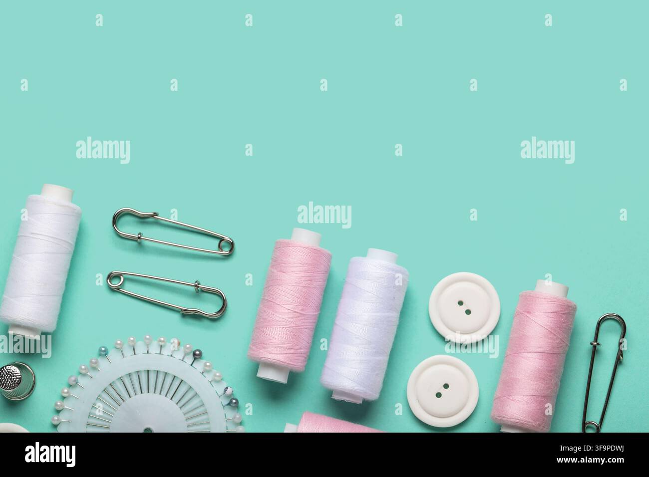 Composition with thread spools, ball pins and buttons on mint background, closeup Stock Photo