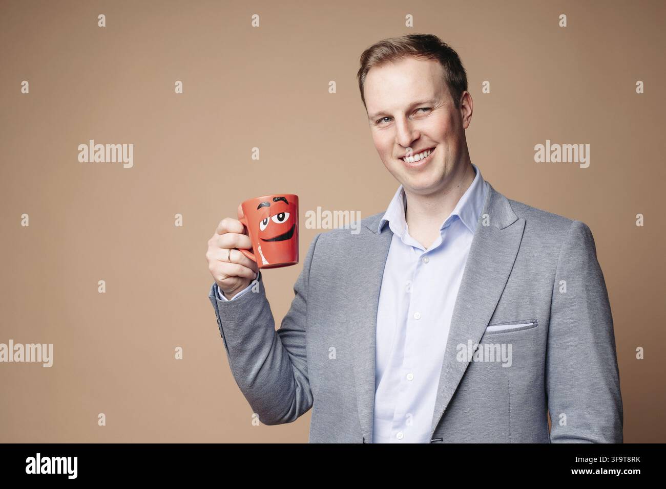 Studio portrait of determined successful businessman in suit and shirt holding red mug with positive slogan Everything is under control . He is smilin Stock Photo