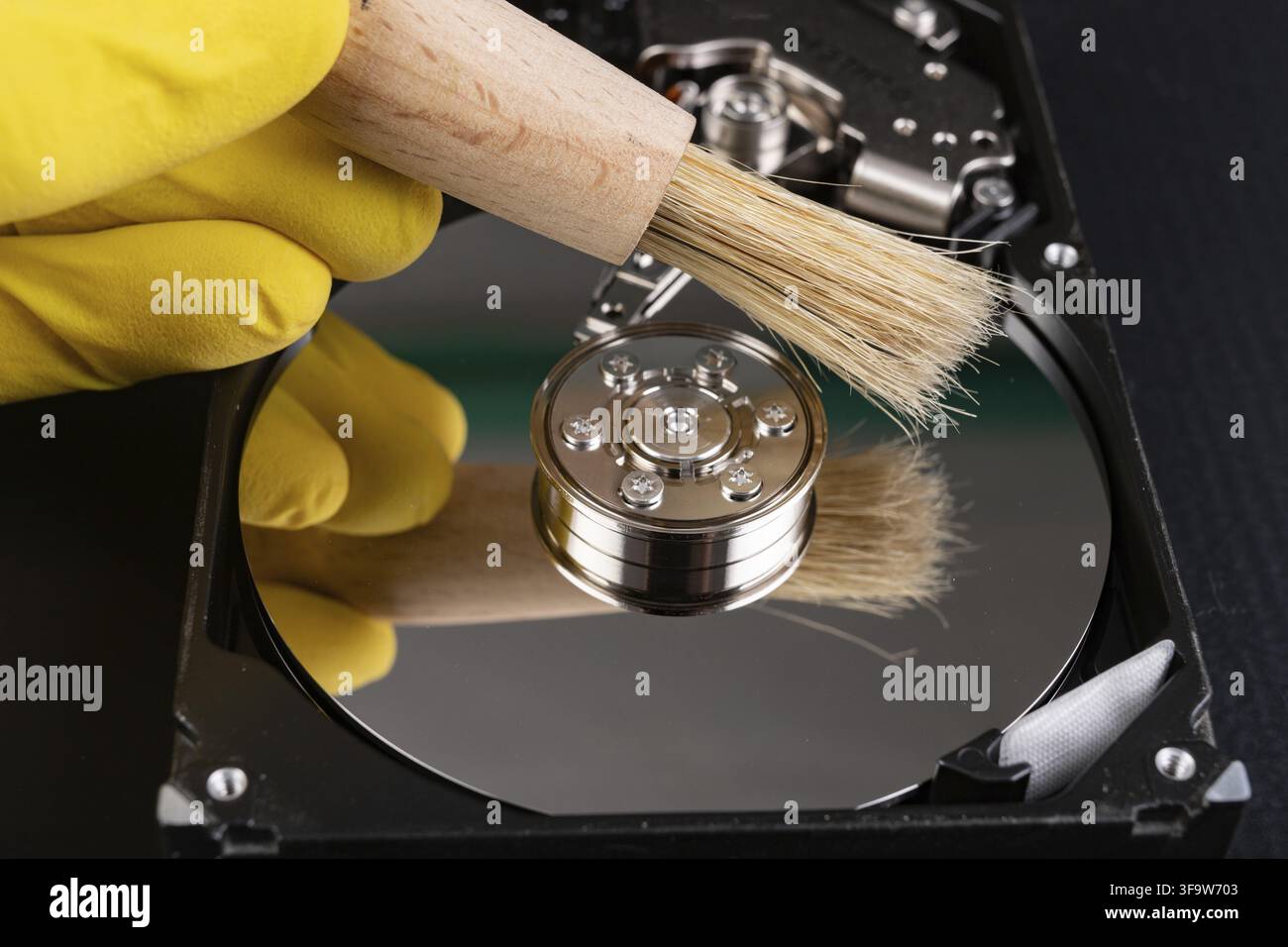 Cleaning the hard disk with a brush. Vacuuming old disk data on your computer. Dark background Stock Photo