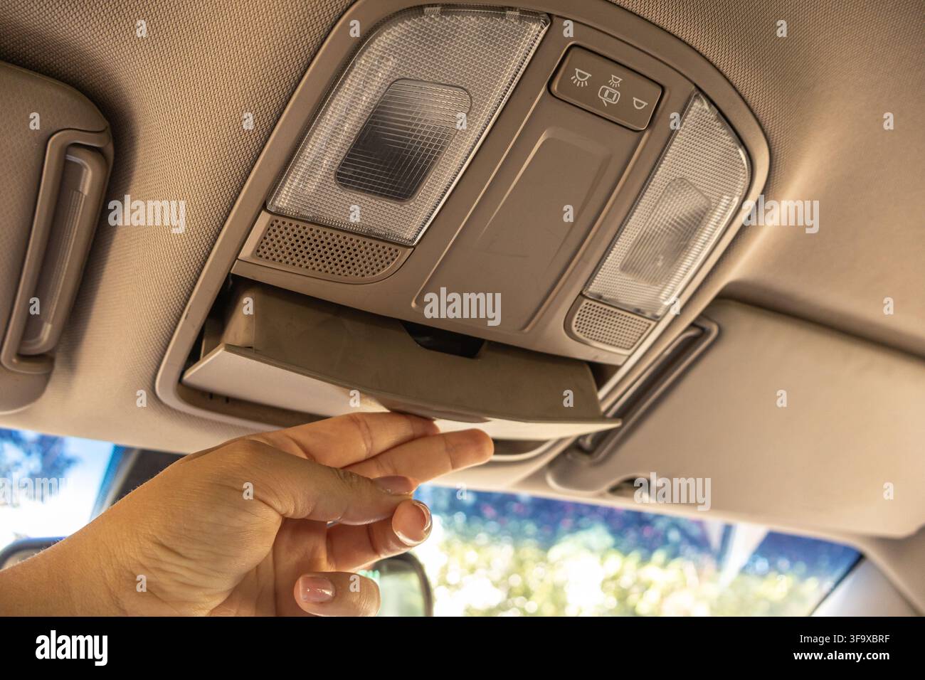 Hand pulling down the overhead sunglass storage compartment built into the car ceiling console. Stock Photo