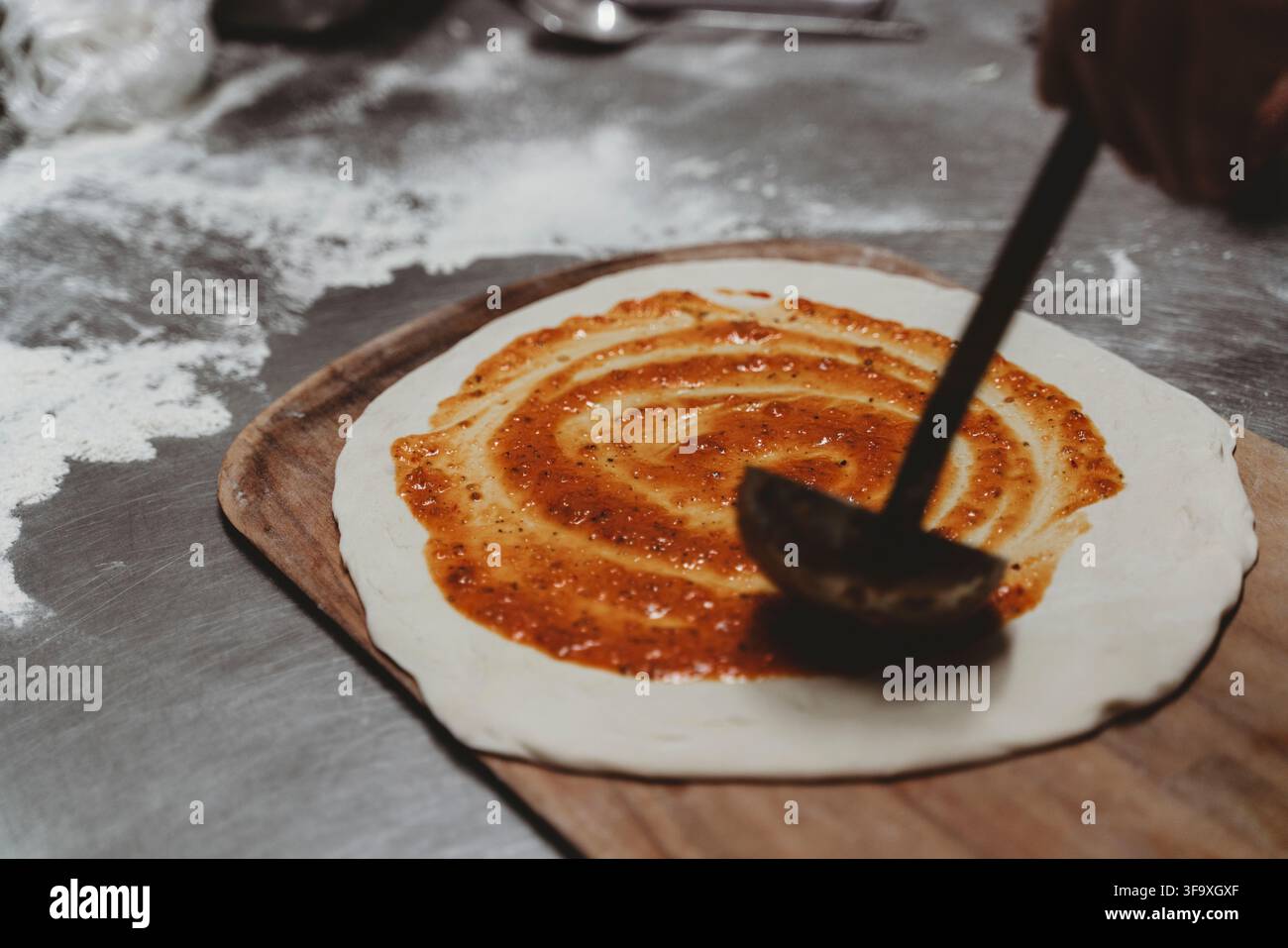 Chef spreading tomato sauce on pizza dough Stock Photo