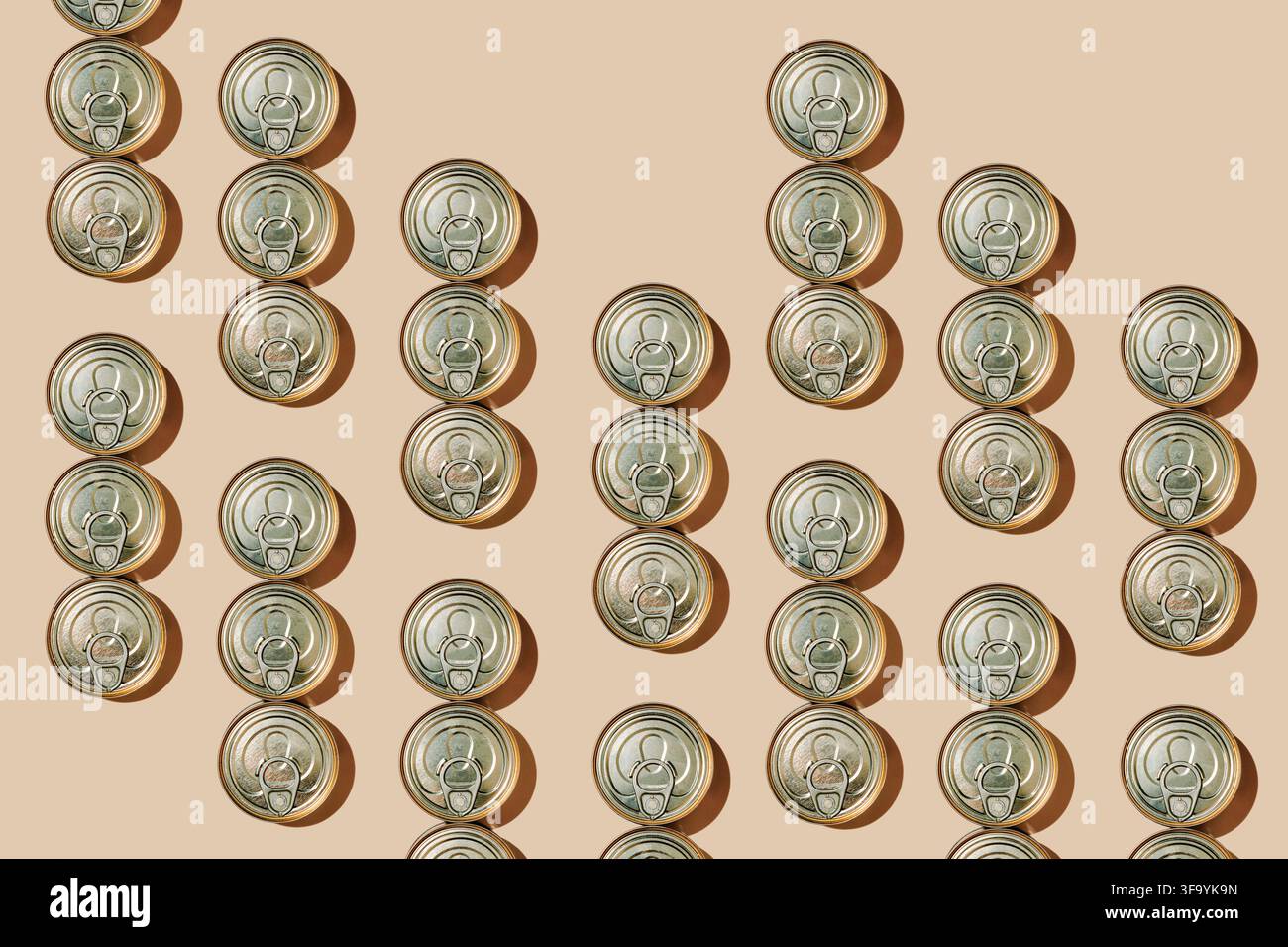 seen from above, numerous unopened food cans with ring pull lids create a loose repeating pattern across a beige background, extending beyond the fram Stock Photo
