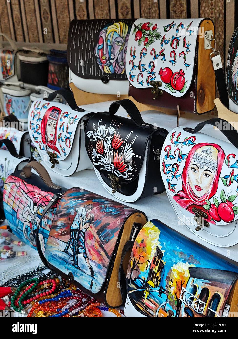Hand-painted leather bags with colorful artistic designs. Each bag features unique, vibrant artwork. Bags are displayed on a wooden surface. Some show Stock Photo