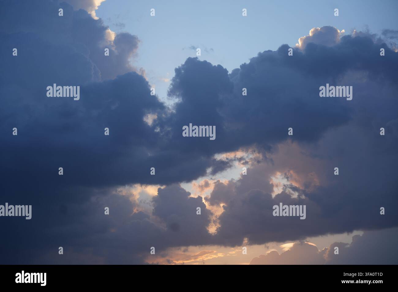 Dramatic sunset glowing behind heavy dark storm clouds and blue sky Stock Photo