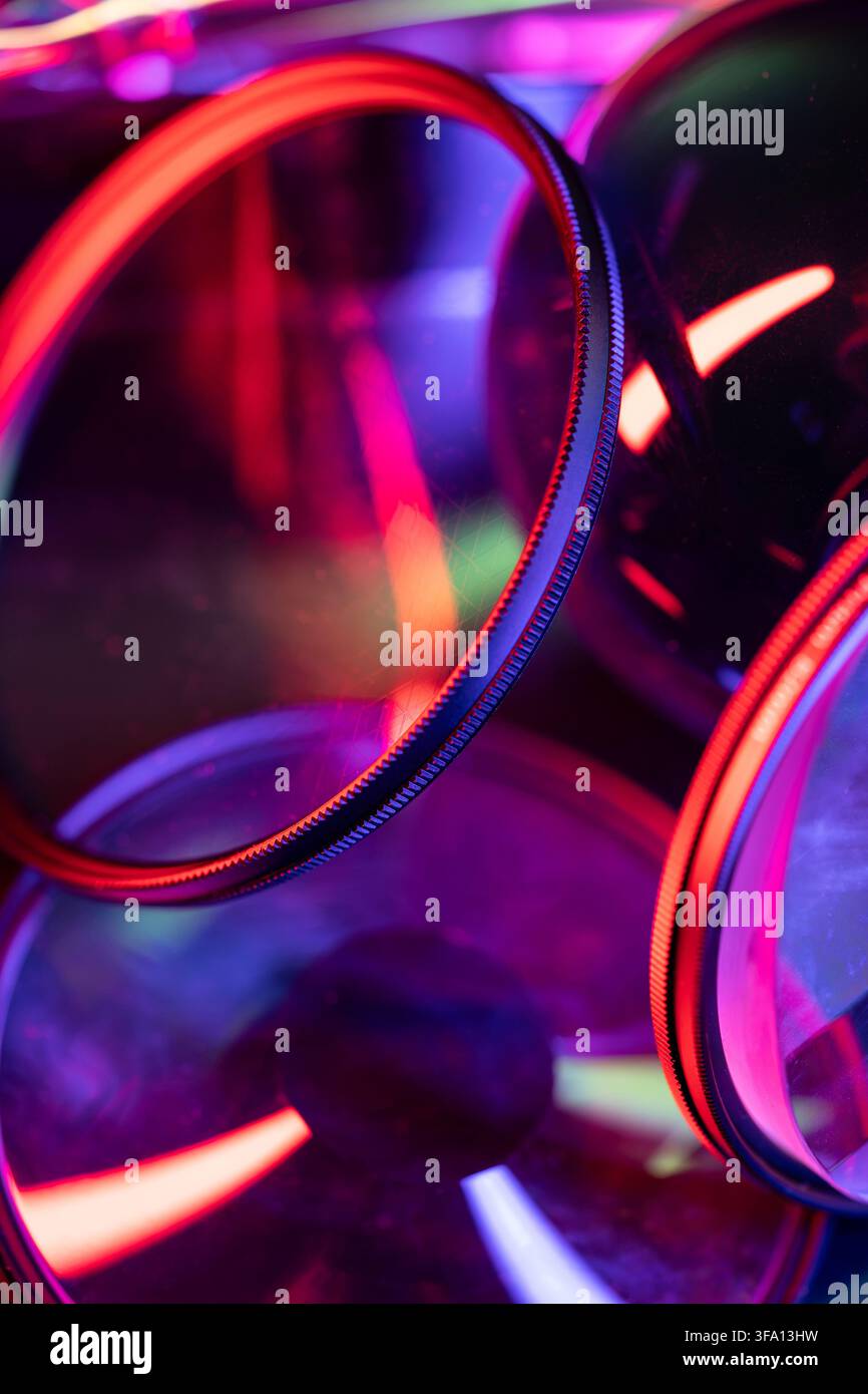 Close-up of overlapping camera lens filters with vivid neon red, purple and blue reflections, creating an abstract futuristic composition for photogra Stock Photo