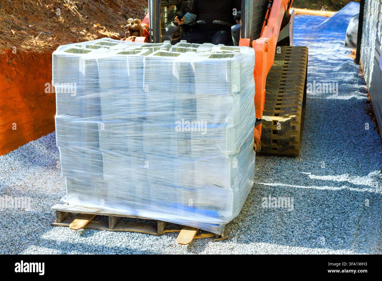Worker uses machine to transport pallet of concrete blocks on gravel at construction site Stock Photo
