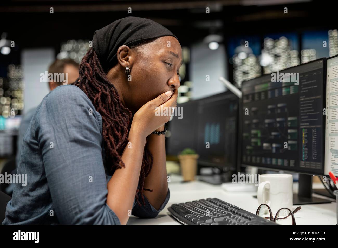 Tired programmer yawns at office desk while working late on computer for tech company. Exhausted software developer feeling fatigue while doing machine learning coding on PC Stock Photo