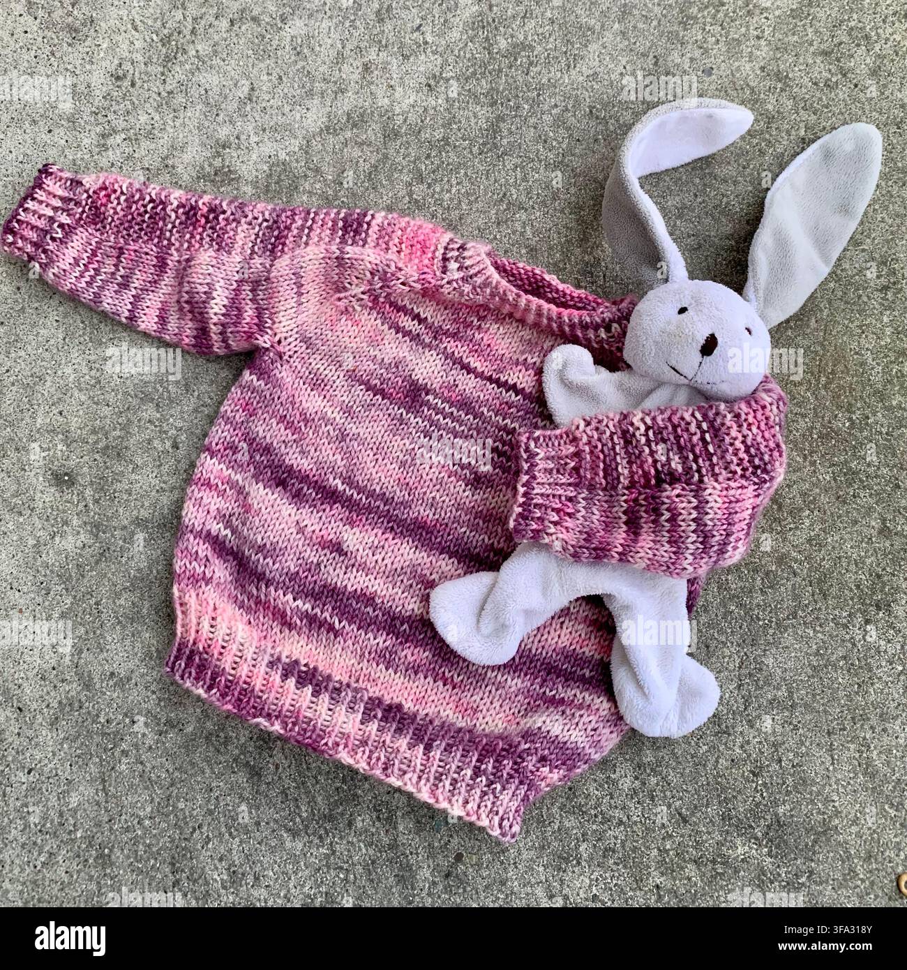 Hand knitted pink hand dyed yarn baby sweater with a white plush toy, cosy handmade baby clothing - Smartphone Captured Stock Image