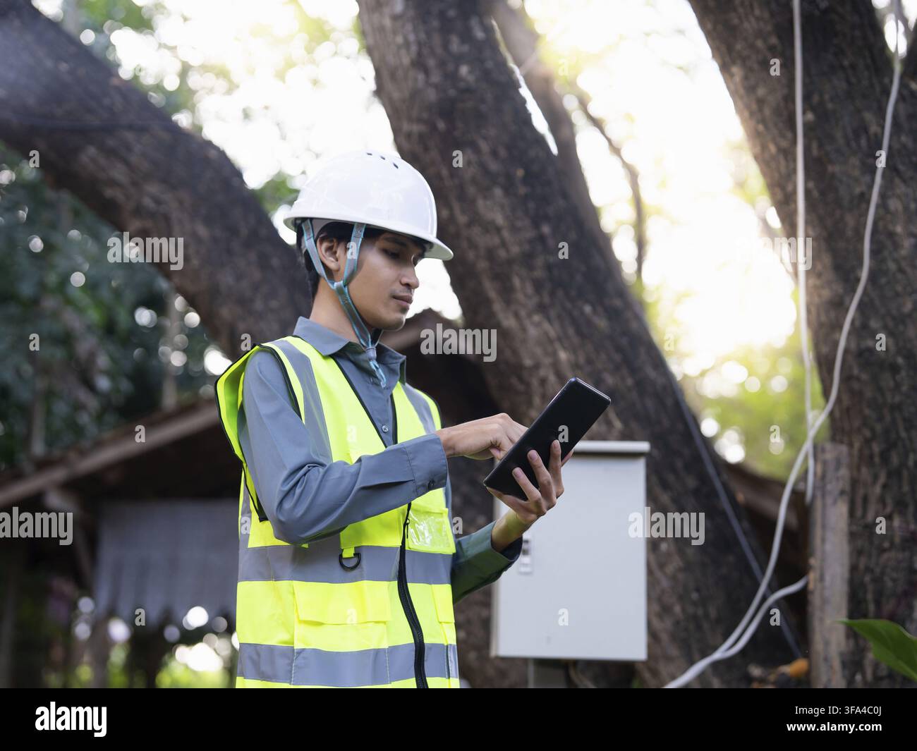Asian electrical engineer using tablet for monitoring power system digital technology representing smart energy management and sustainable future Stock Photo