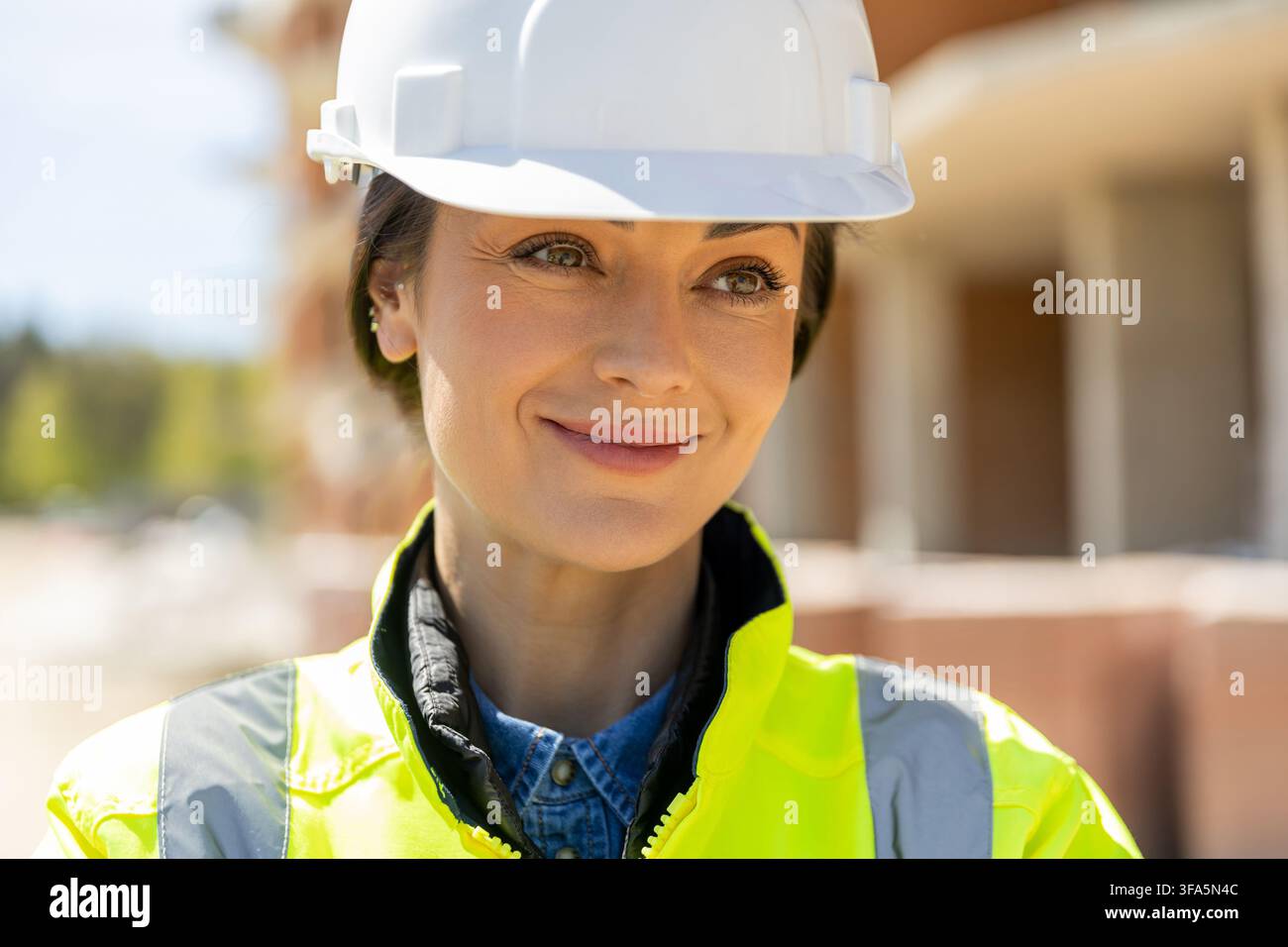 Professional female builder wearing protective hard hat looking away Stock Photo