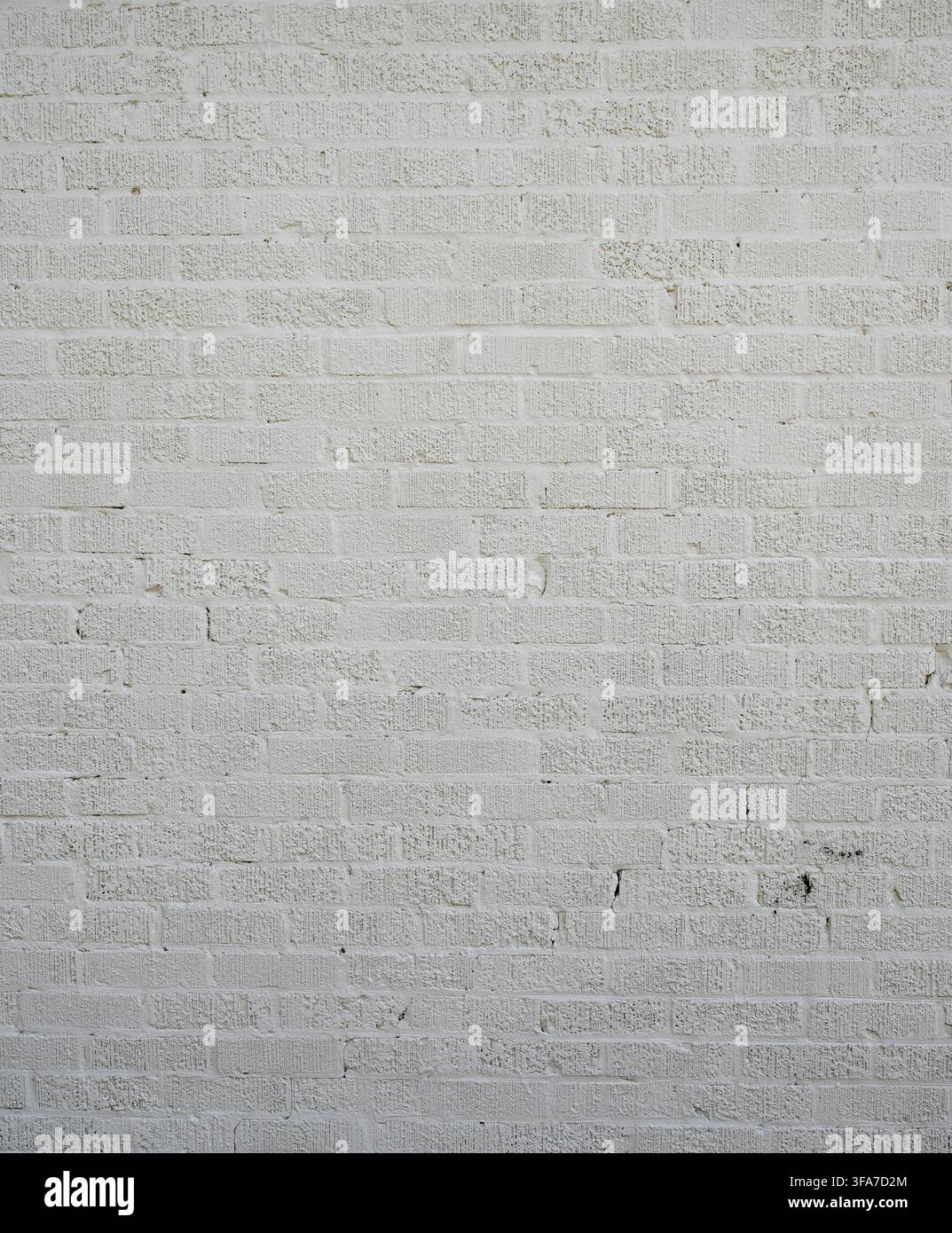 Vertical close-up view of a white painted textured brick wall surface with rough chipped bricks with grooved faces Stock Photo