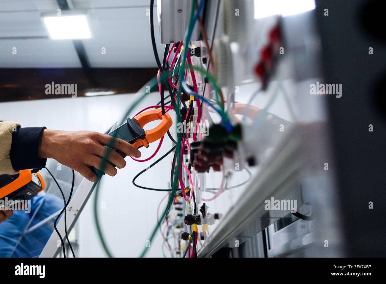 echnician using a clamp meter to measure electrical current in a solar training system. Stock Photo