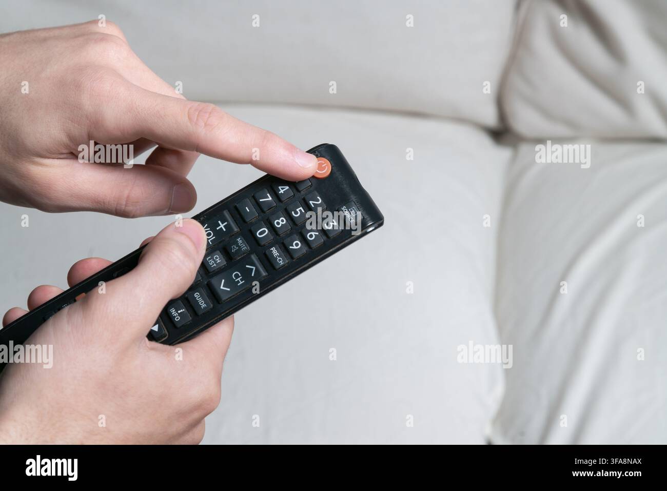 Person's hand pressing power button on a universal remote controller for television Stock Photo