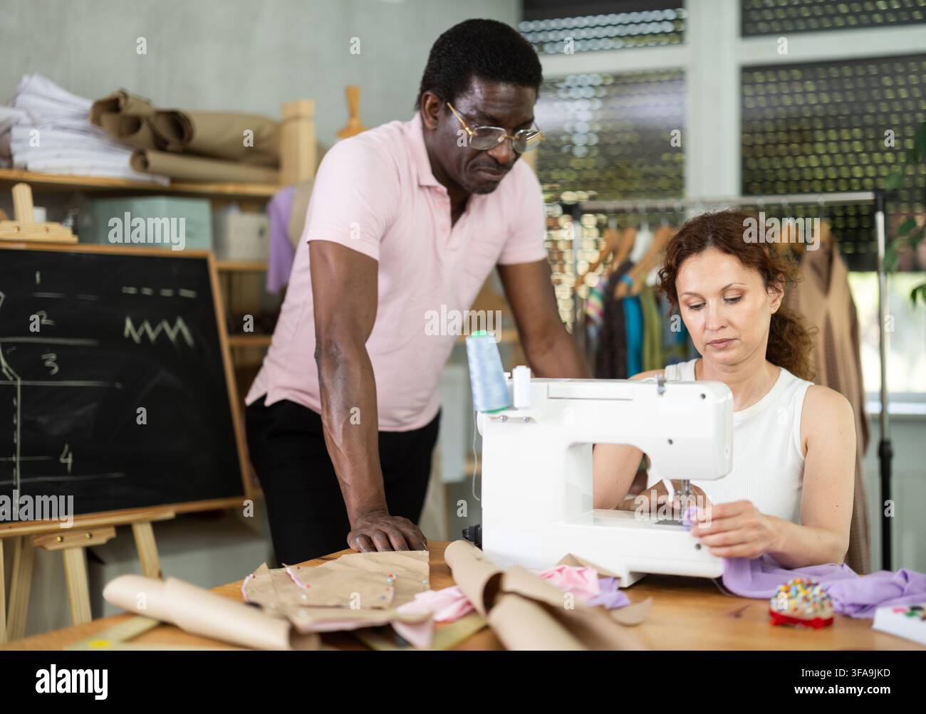 Middle-aged male teacher helping students sew Stock Photo