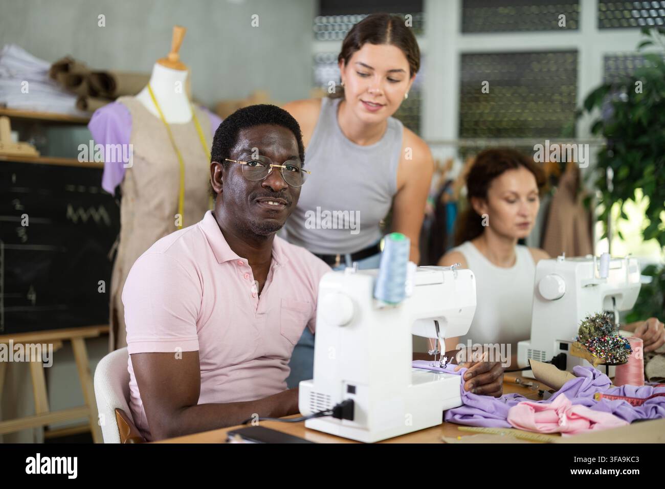 Middle-aged female teacher helping students sew Stock Photo