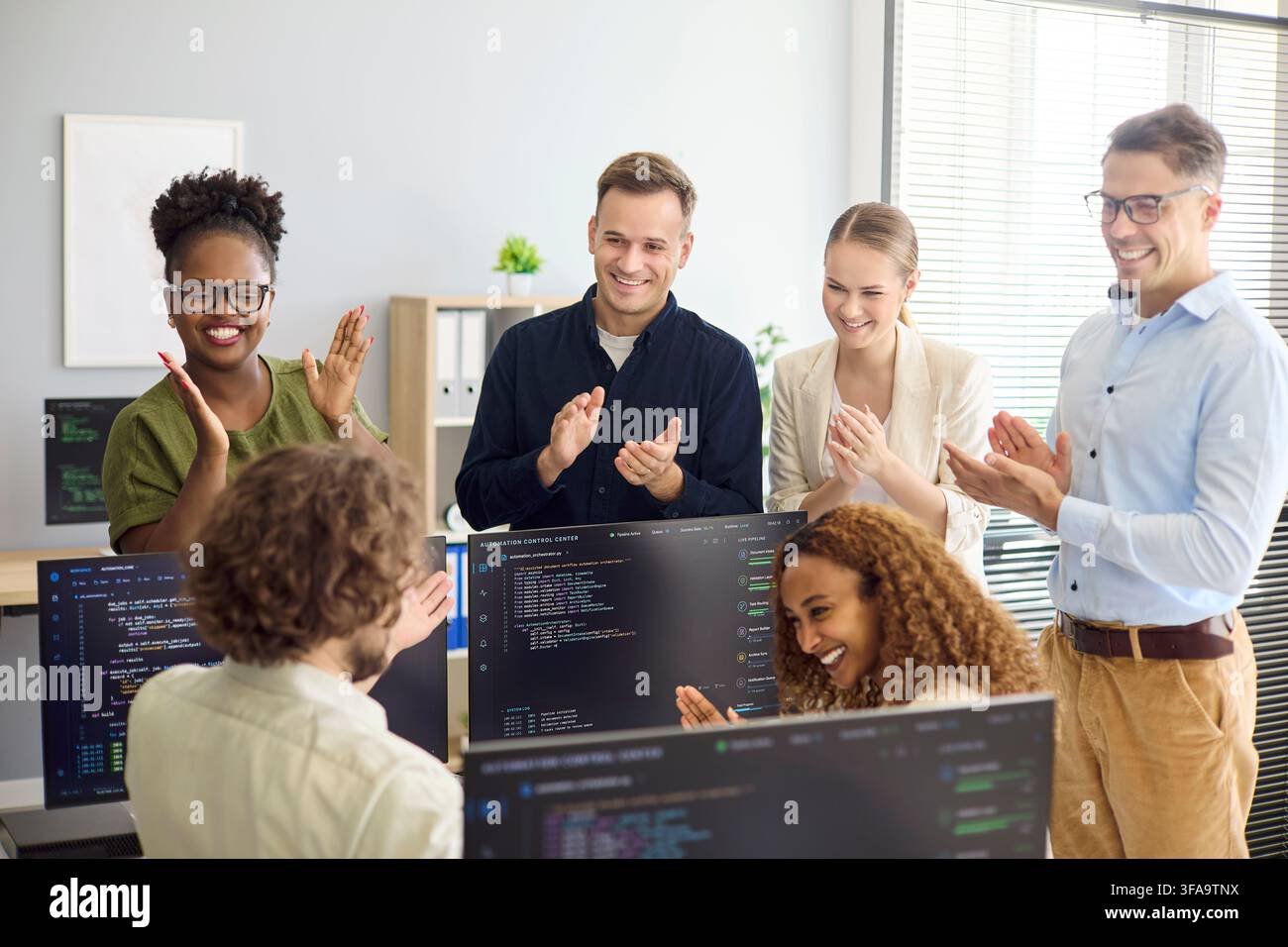 Diverse developer team applauding successful code release in modern office meeting Stock Photo
