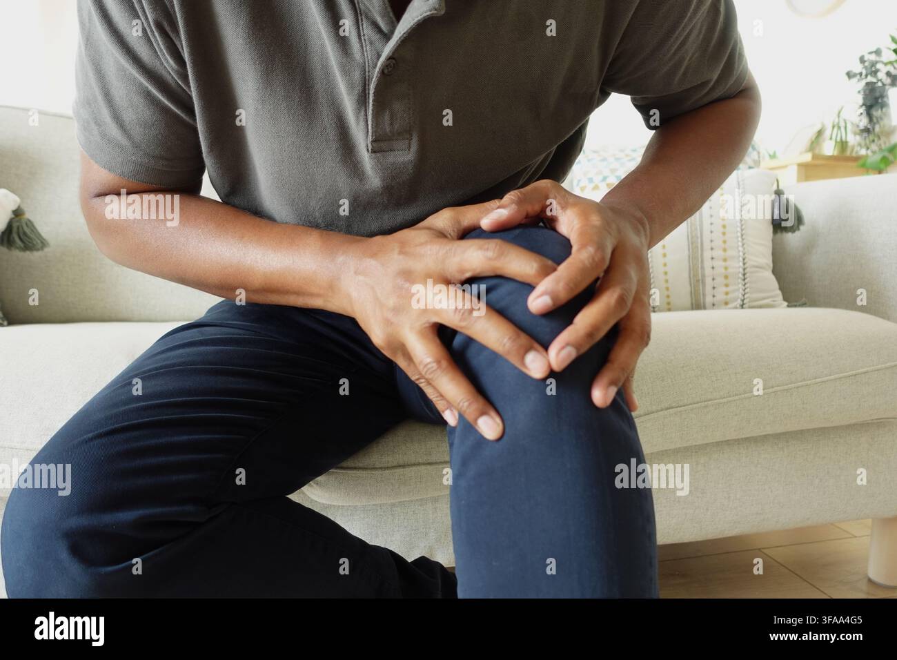 Man holding his knee while sitting on a couch Stock Photo