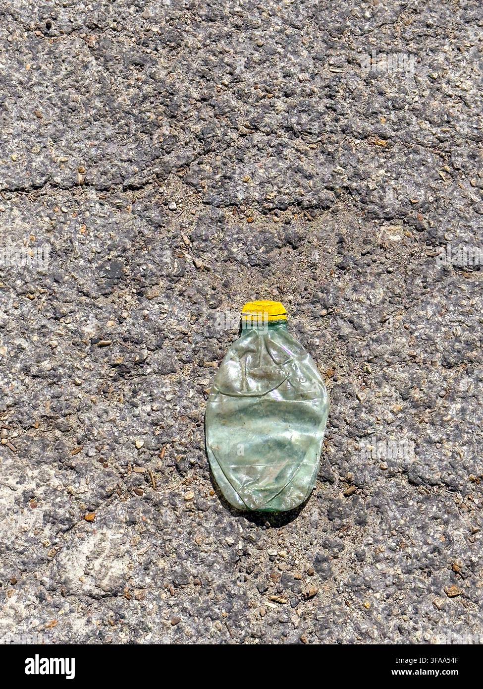 Mexico, 2026. A crushed discarded plastic bottle lies on rough asphalt, a stark image of single-use plastic waste, litter and the environmental impact - Smartphone Captured Stock Image