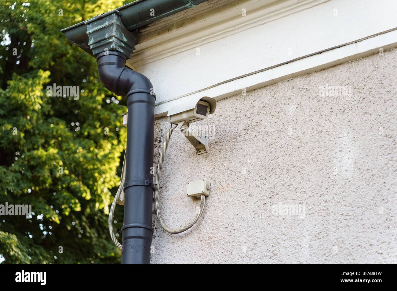 Security camera installed on a textured building wall beside a drainpipe for surveillance, monitoring, and perimeter safety protection, safety technology Stock Photo