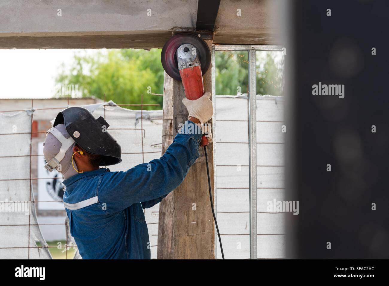 Construction worker using an angle grinder on a building structure outdoors Stock Photo