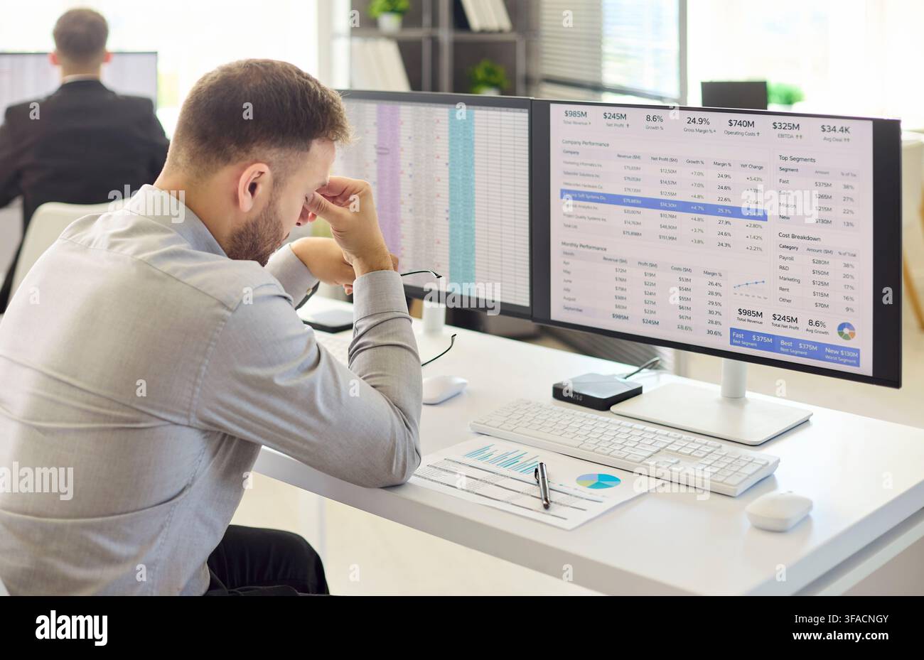 Stressed financial analyst man at computer in modern office with spreadsheets Stock Photo