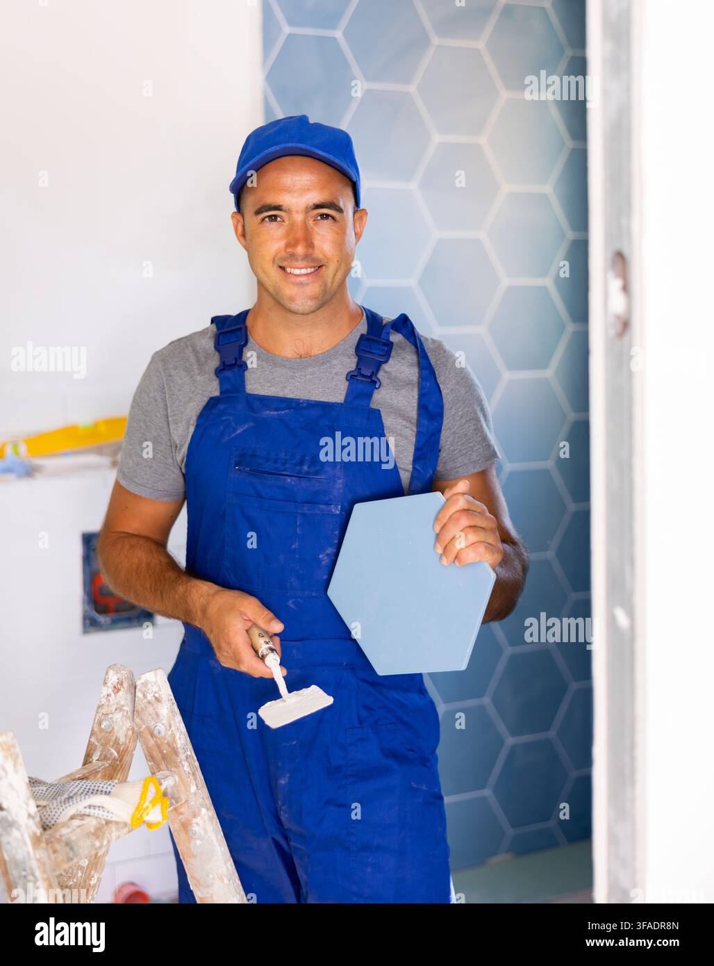 Skilled builder in work clothes posing with ceramic tiles and construction tools while repair and decoration in apartment Stock Photo