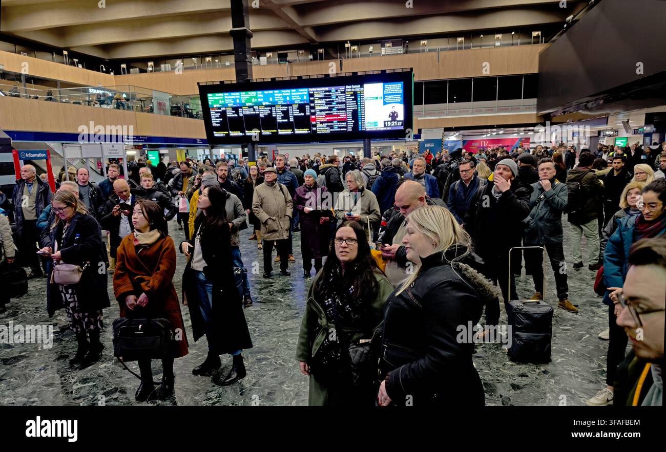 Passengers waiting beneath departure boards at London Euston station, illustrating crowding and uncertainty at a major Network Rail terminus. Stock Photo