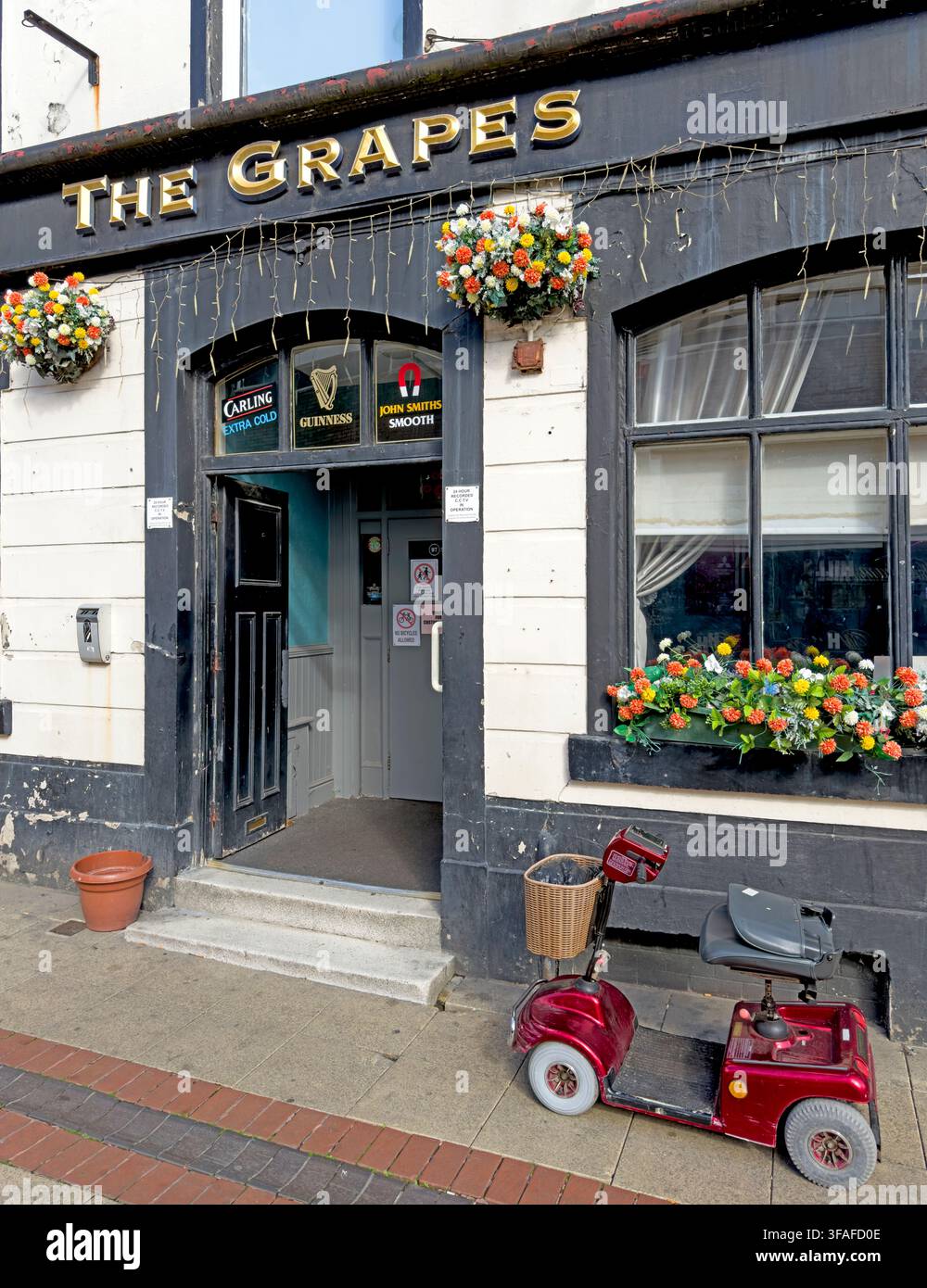 Entrance of The Grapes pub, 27 Church Street, Eccles, with flowers, grab rails and a red mobility scooter outside, Salford, England, UK. Stock Photo