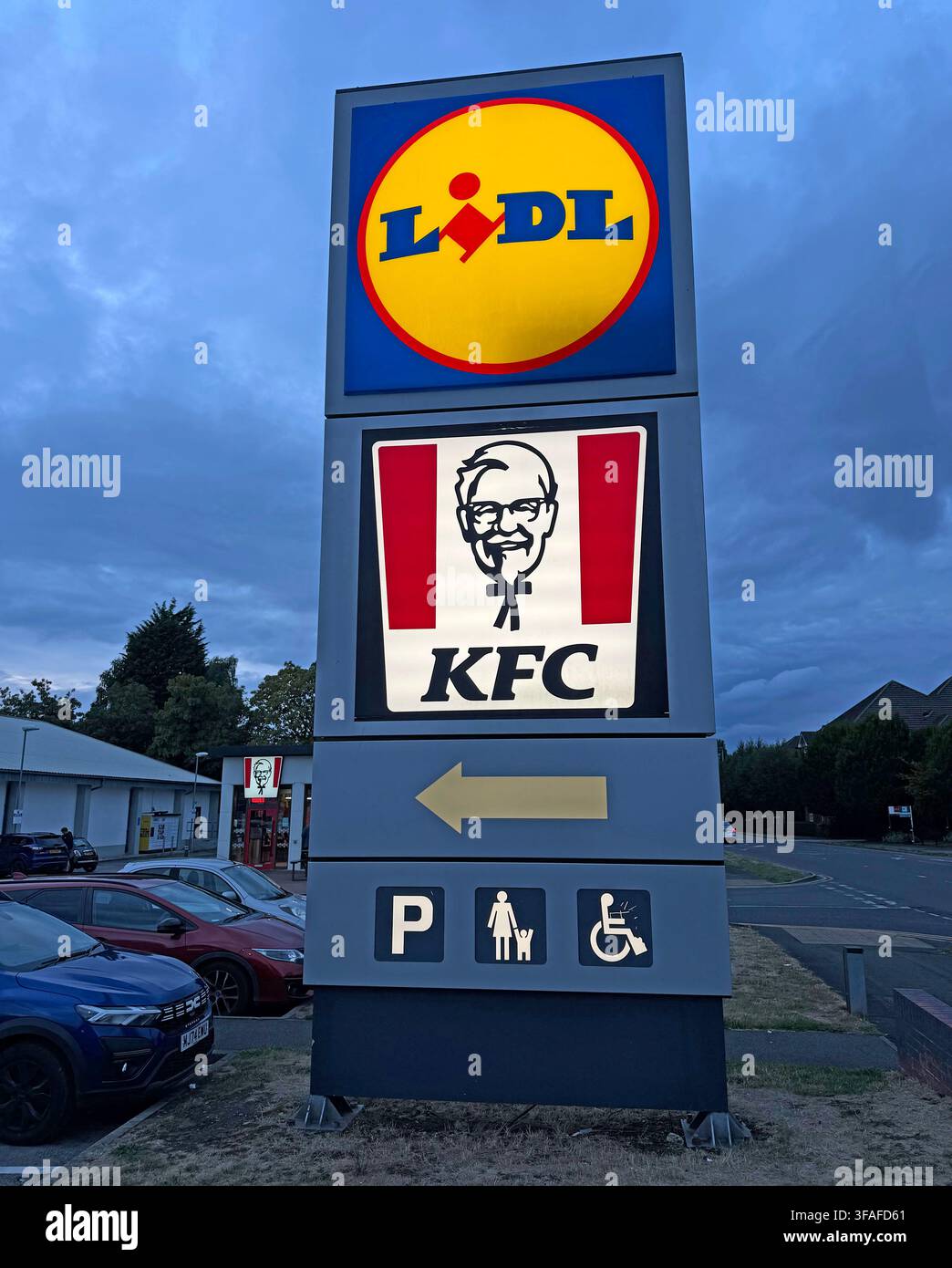Lidl and KFC roadside signs at dusk on Thelwall Lane, Latchford, Warrington, combining discount retail and fast-food brands. Stock Photo