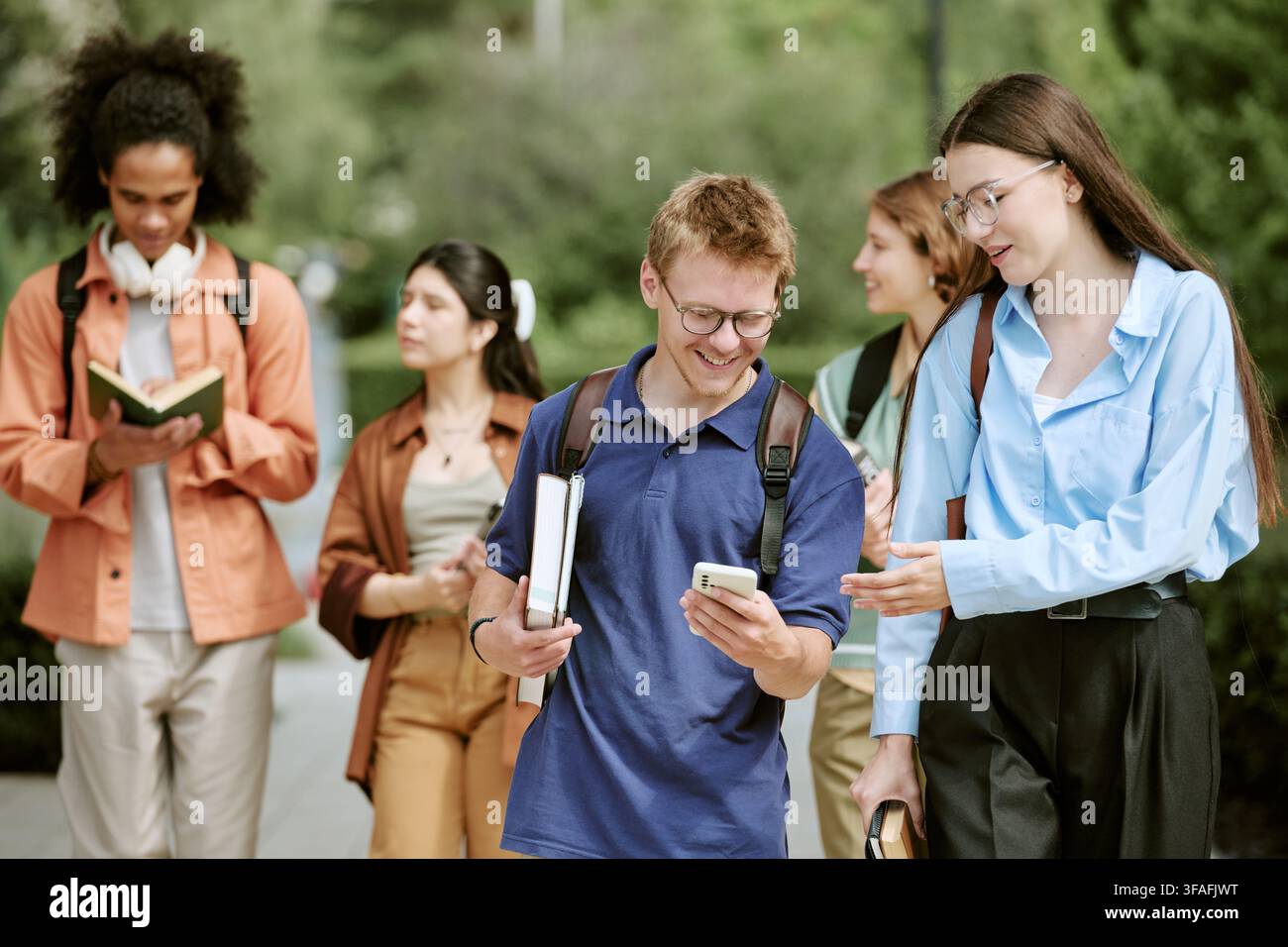 Diverse Students Walking on Campus and Looking at Smartphone Stock Photo