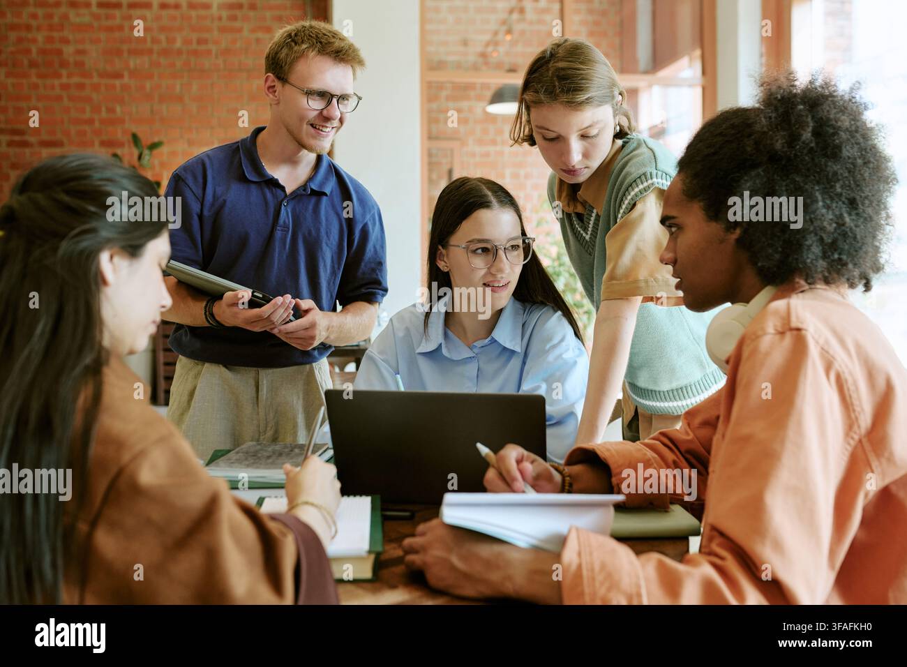 Diverse Students Collaborating on Group Project with Laptop in Campus Cafe Stock Photo