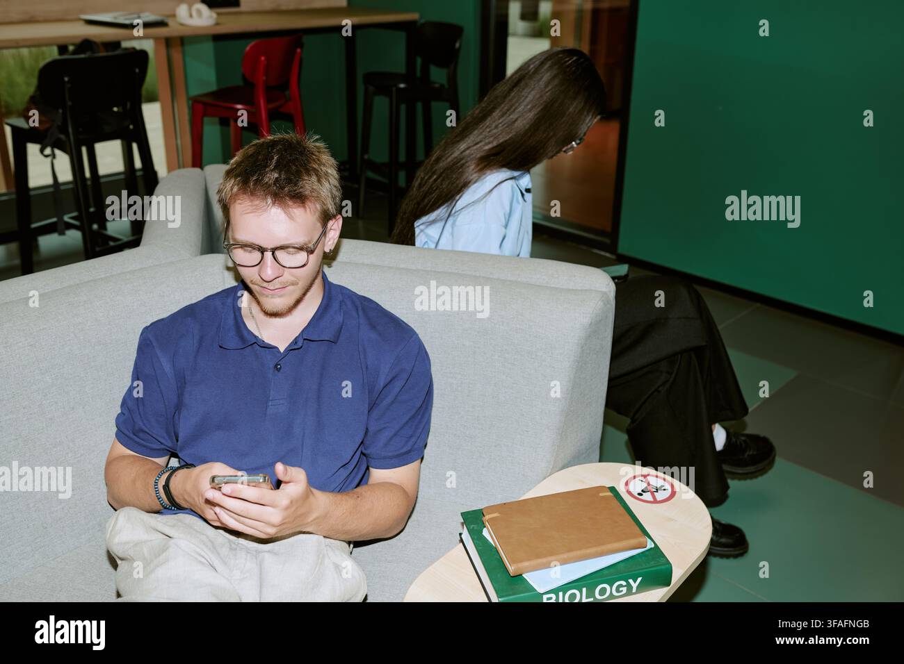 Diverse Students Using Smartphones on Sofa in University Campus Lounge Stock Photo