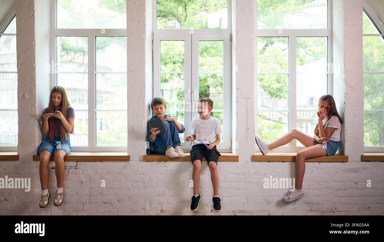 Four children using smartphones separately while sharing window seat Stock Photo