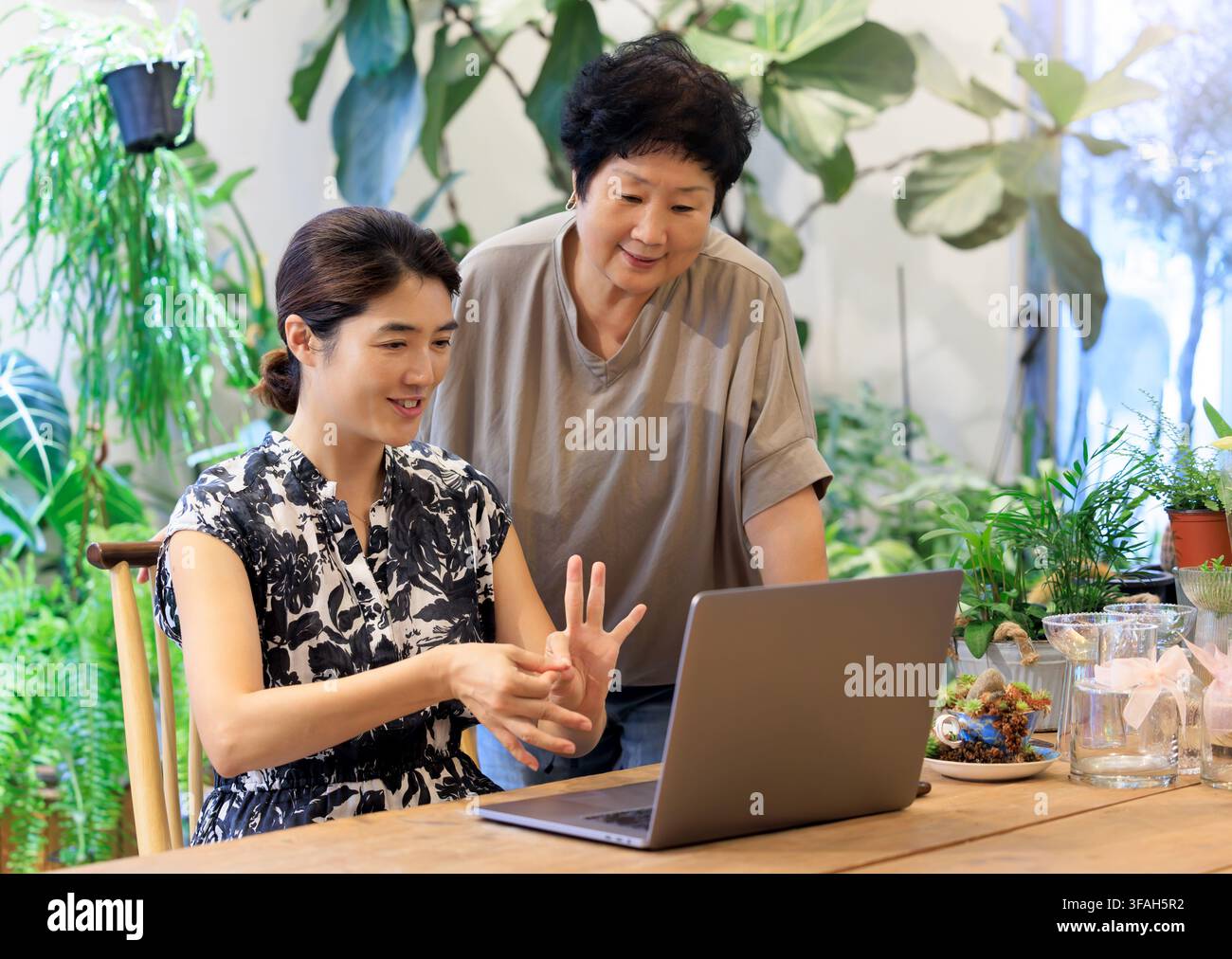 Two Korean Women Using Sign Language While Watching a Laptop Together Stock Photo