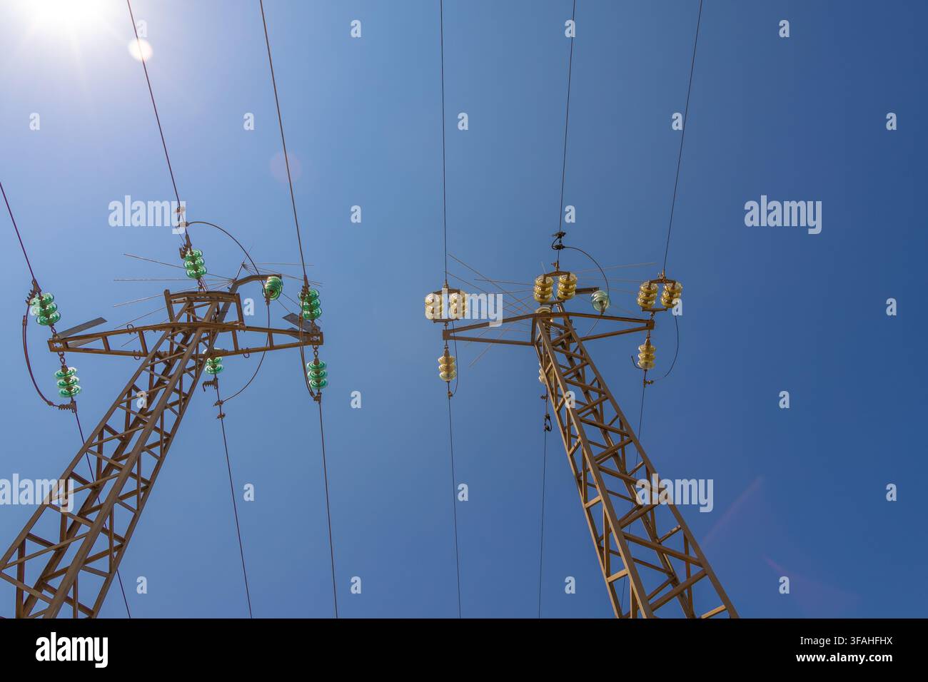Low angle view of two tall electricity pylons supporting high voltage power lines under a clear sunny sky Stock Photo