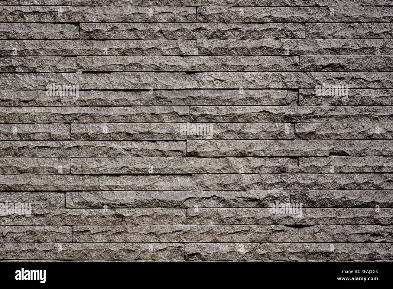 Close up of a dark grey textured stacked stone wall. A modern natural stone veneer cladding surface ideal for architectural and interior design. Stock Photo