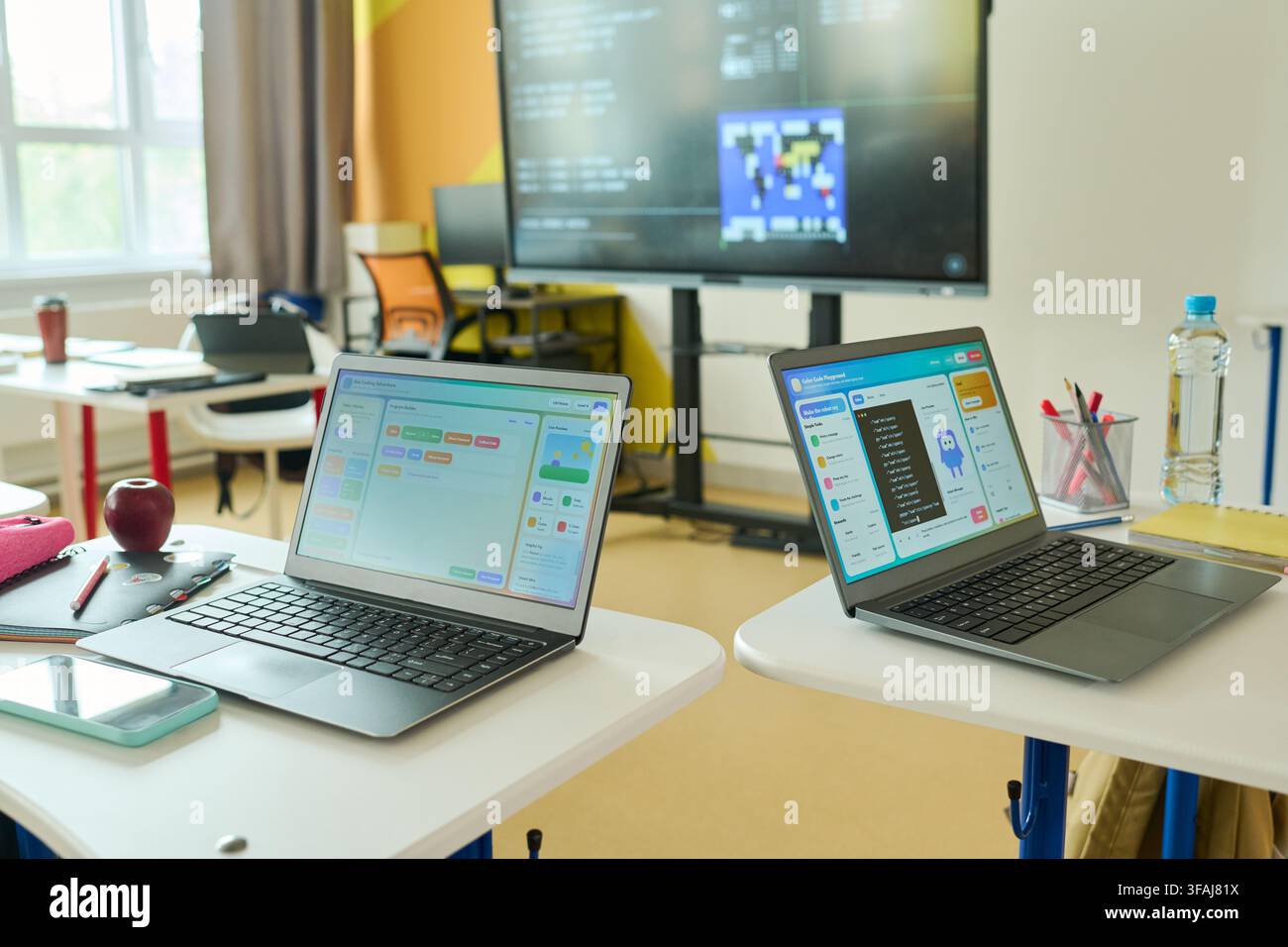 Laptops Displaying Coding Software on Desks in Empty Classroom Stock Photo