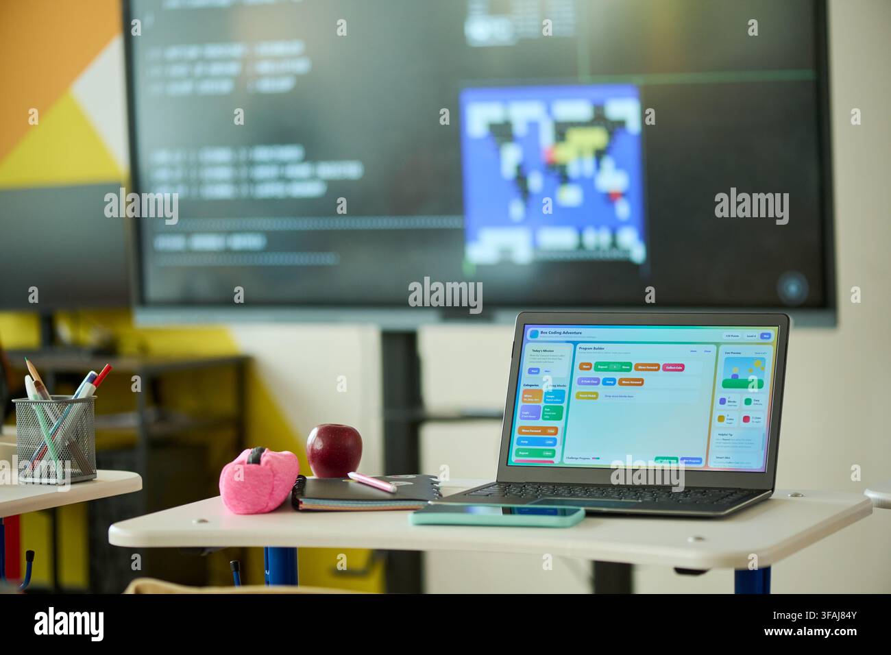Laptop Displaying Coding Software on Desk in Modern Classroom Stock Photo